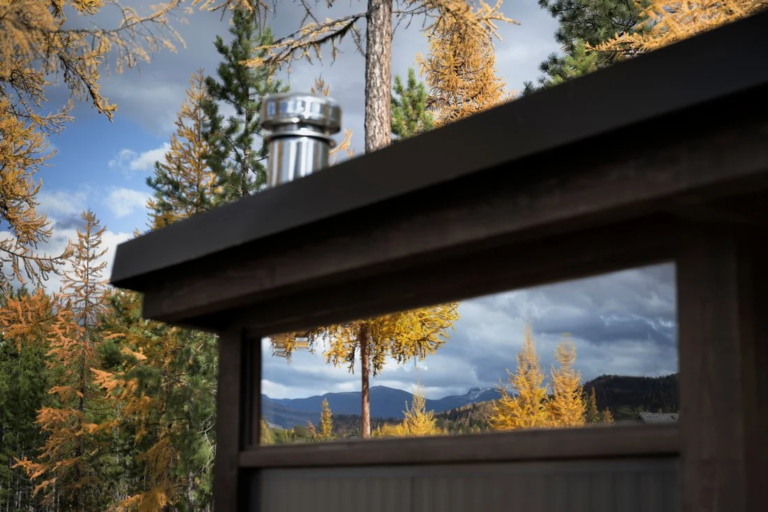 Mettä sauna transom window reflecting larches and mountains, Kootenays, BC