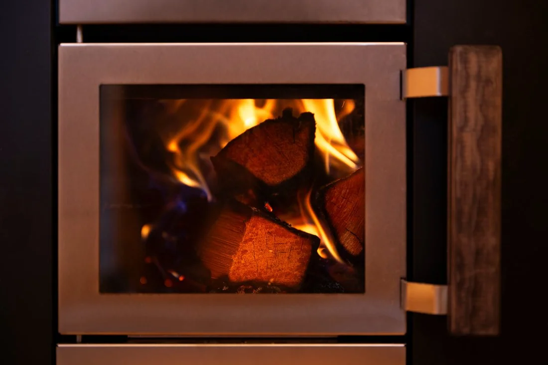 Wood fire burning in a sauna heater with stainless door and wood handle