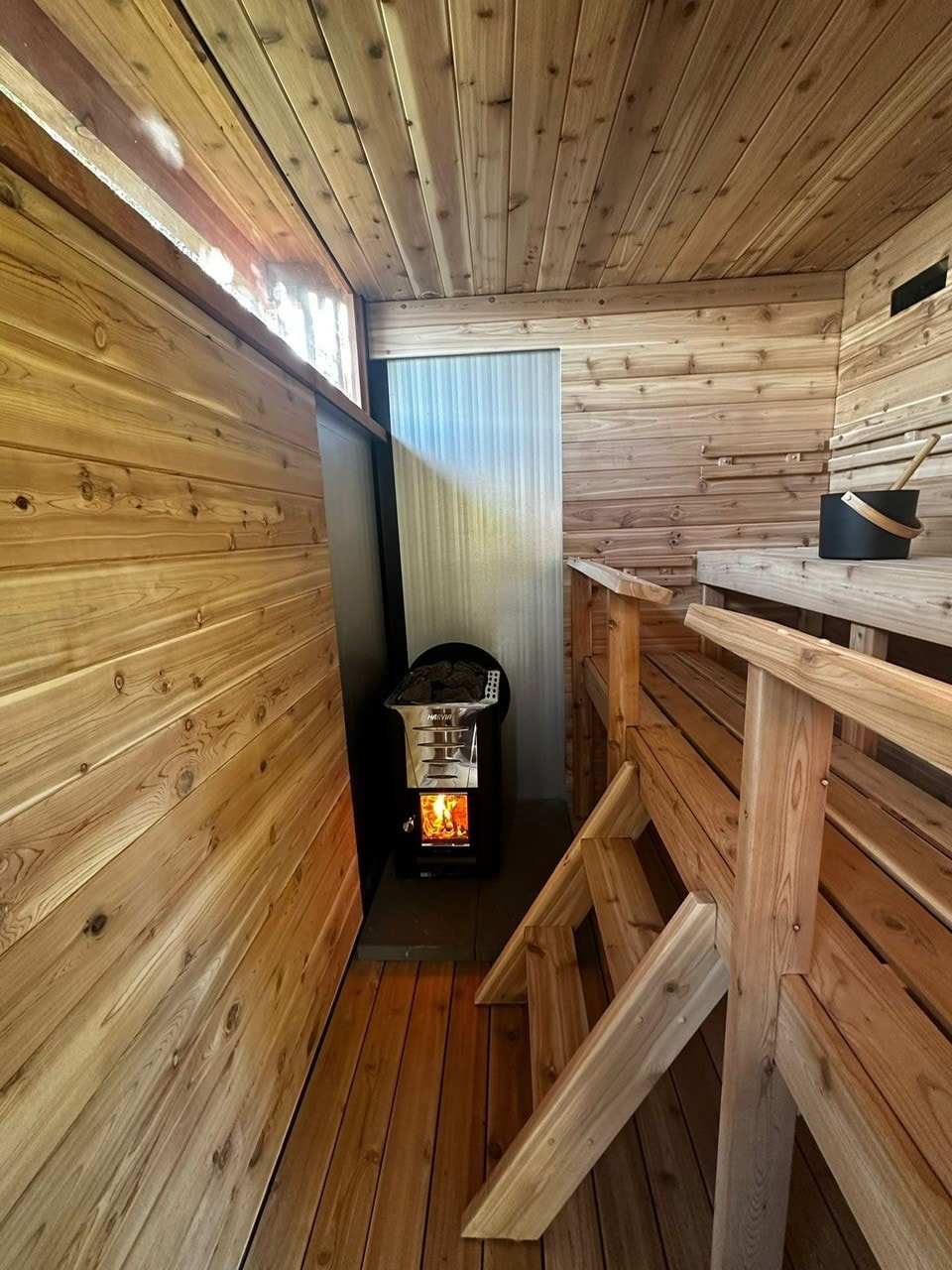 Cedar-lined Kamu sauna interior with wood-burning heater and high benches
