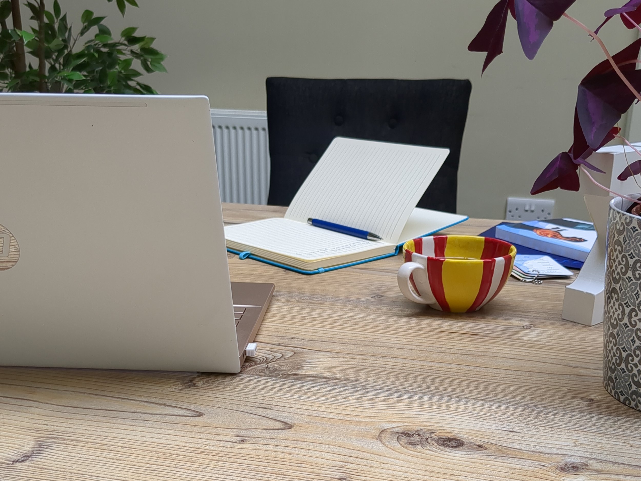 Image of a desk with an open notebook and open laptop, but no person sitting in the chair, as if someone just stepped away to boil the kettle mid conversation