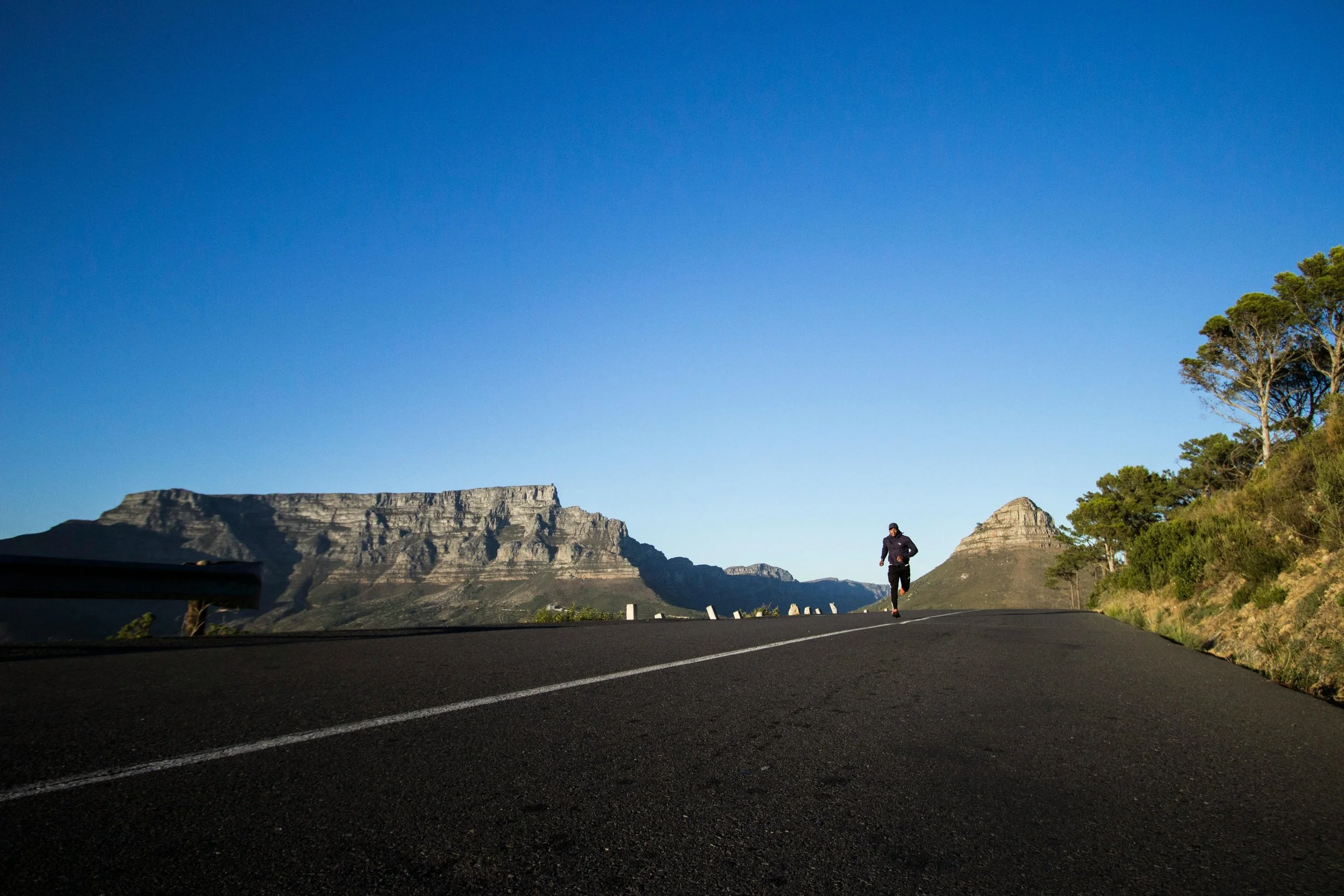 A man jogging on a dirt road in a rural landscape with green grass and trees under a partly cloudy sky.