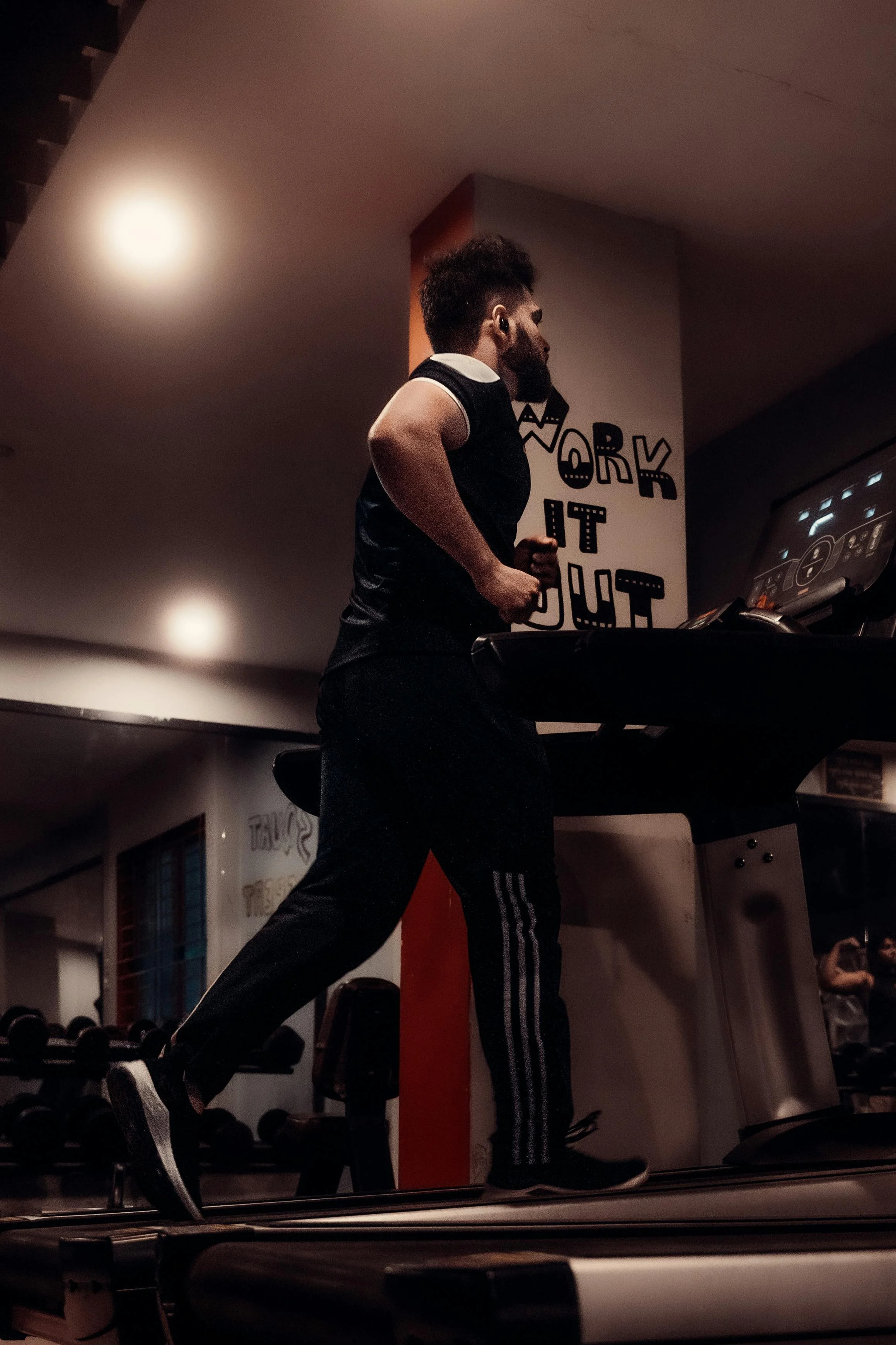 A woman running indoors against a white wall, wearing a white sports bra, white shorts, and running shoes.