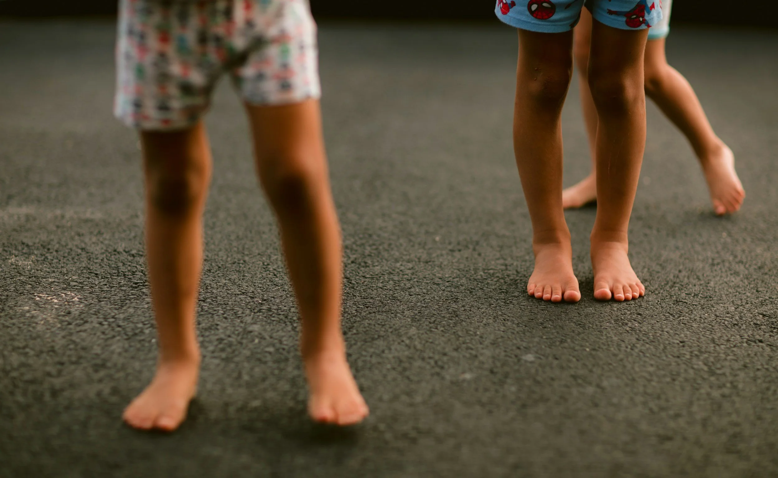 Two young children walking barefoot outdoors, showing their bare legs and feet