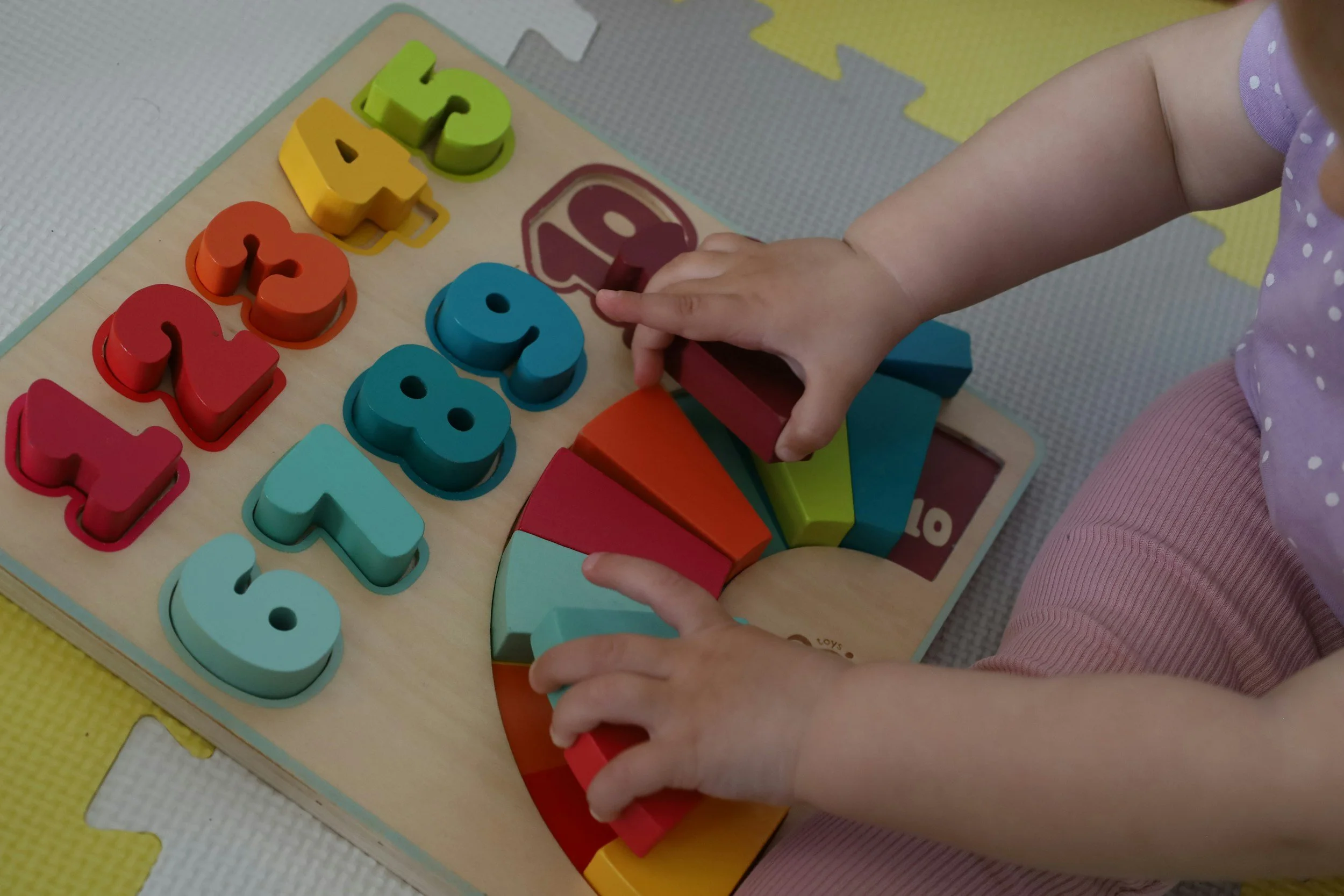 Child's hands arranging colourful wooden number tiles on a puzzle board