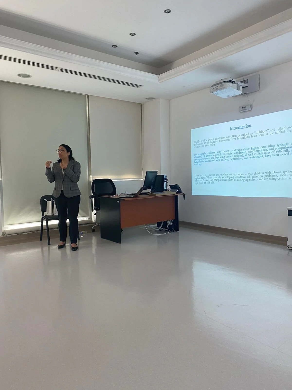 A woman giving a presentation in a conference room with a projected slide on the wall.
