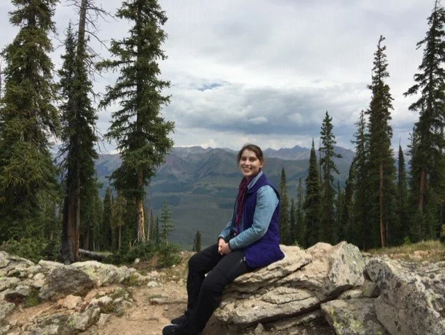 Lia Winnard, a recreation therapist, sitting in front of trees and a mountain.