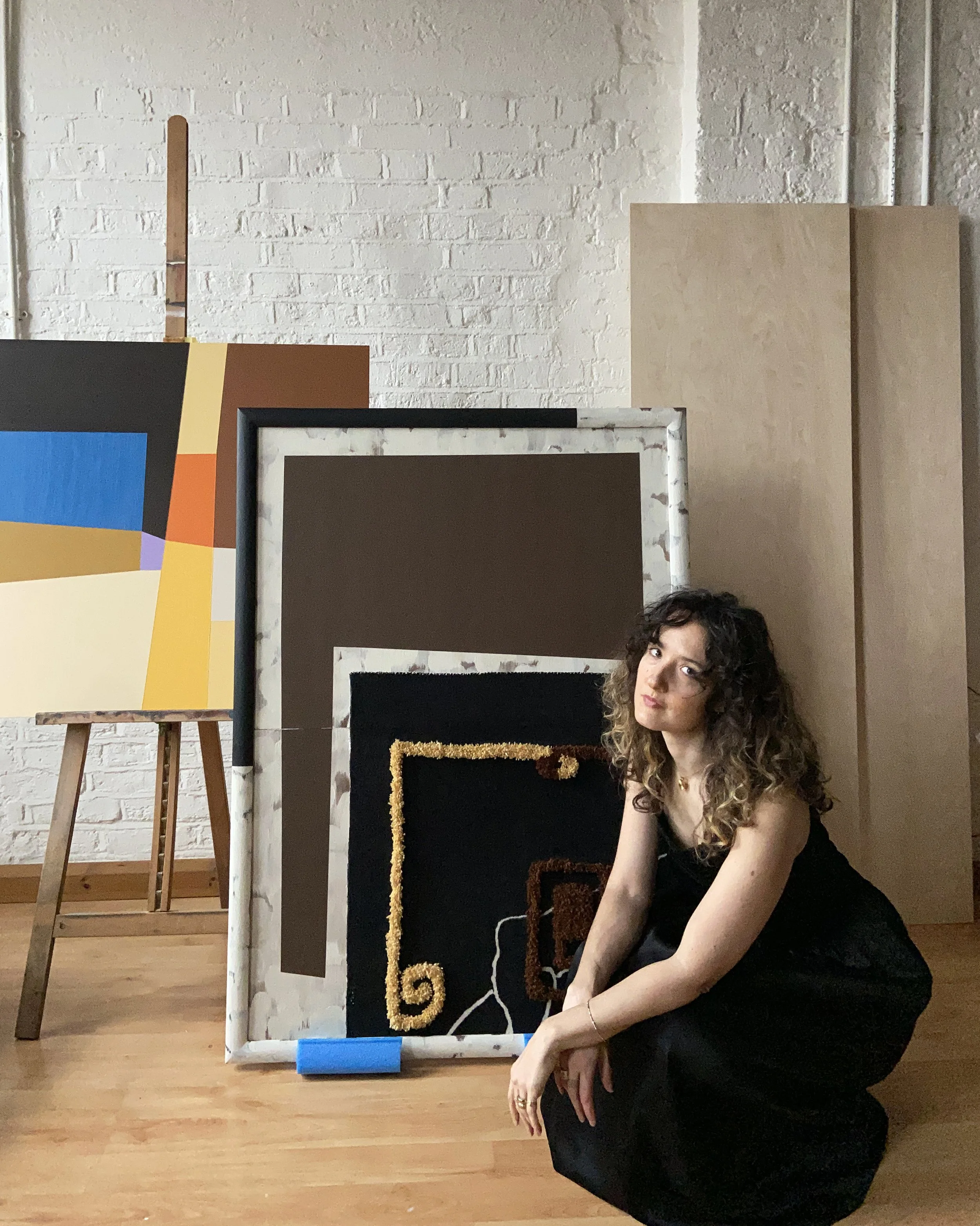London artist and designer Eleanor Nadimi in her studio, seated beside abstract paintings and a tufted textile artwork.