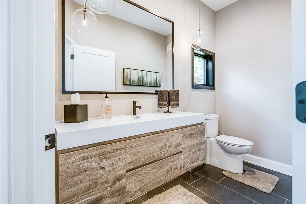 A renovated bathroom with a one-piece sink, rustic wood cabinetry, and large slate tile.