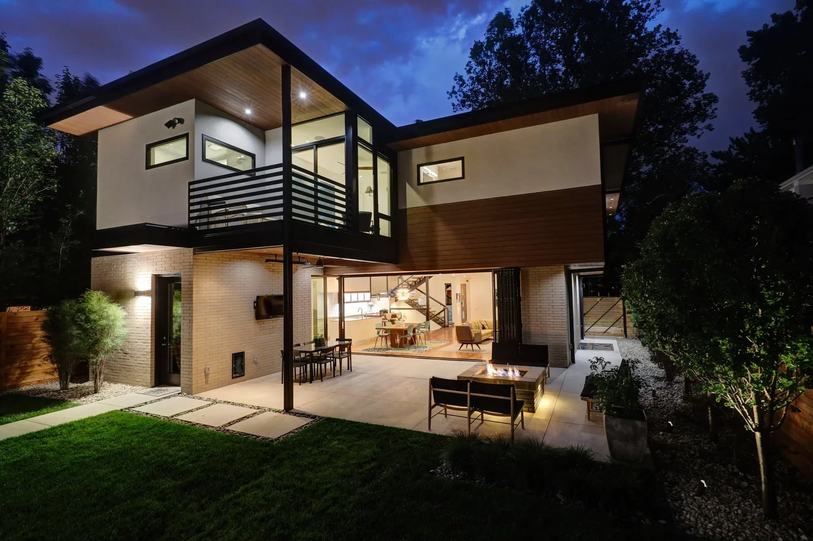 Back exterior of a custom home featuring seamless indoor-outdoor living, a covered patio, and a master bedroom balcony.