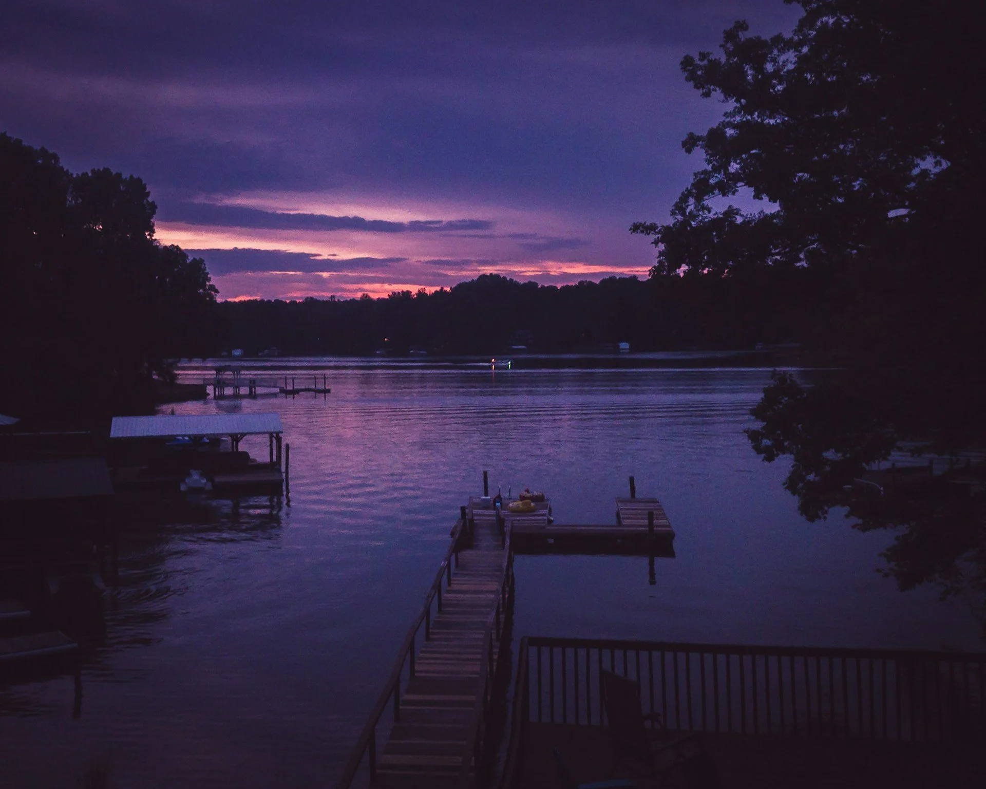 A dock and boathouse at sunset on Lake Norman, NC, with a purple and orange sky.