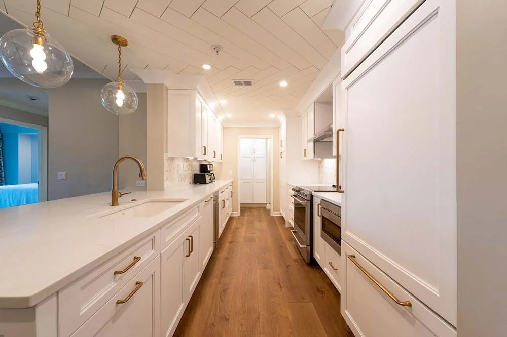 A modern, white, galley kitchen with modern globe lighting and decorative ceiling.