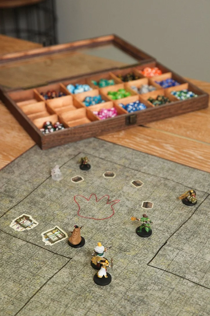 A dungeons and dragons game set up with the characters in a circle around a fire on the board with colorful dice in boxes in the background during a group therapy game in Brentwood, TN.