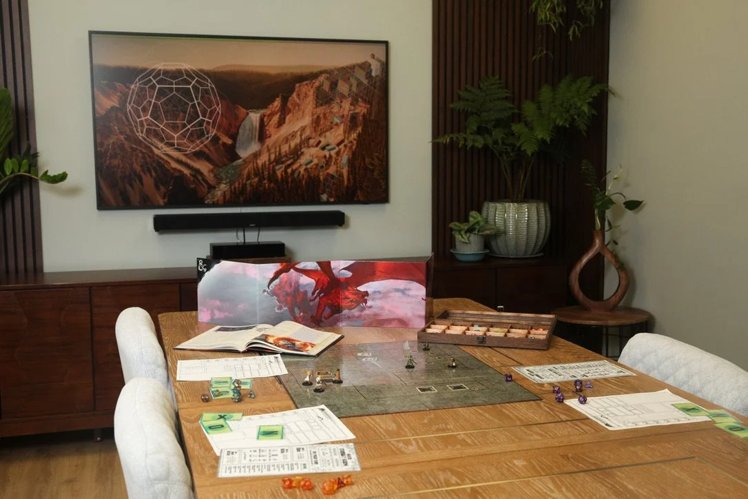 A large group therapy room with a telivision screen showing a beutiful animated waterfall in the background with a dungeons and dragons boardgame set up on the wodden table in the center of the room during dungeons and dragons group therapy.