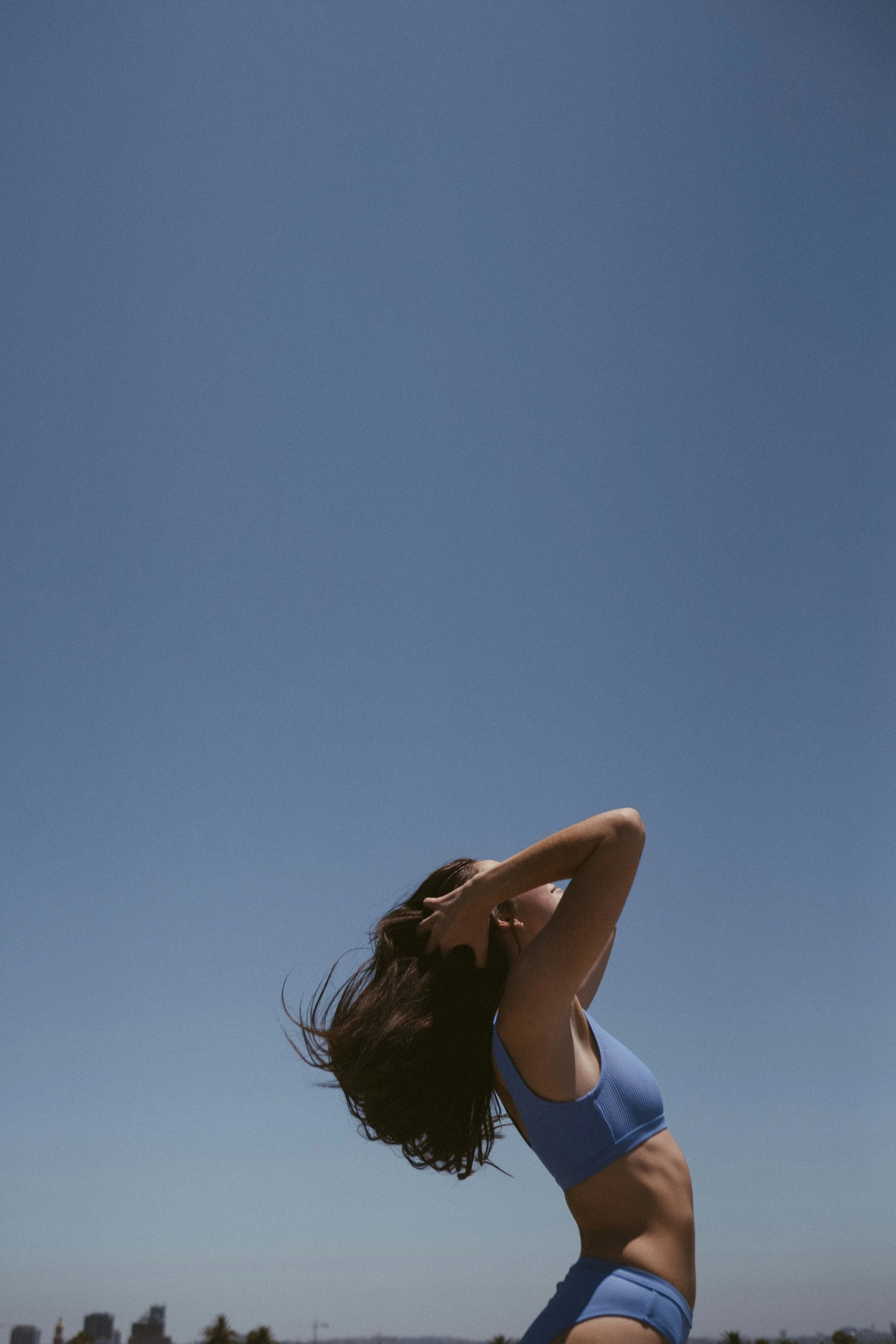 Mujer joven con ropa deportiva ajustada posando bajo un cielo despejado, con cabello suelto y haciendo una pausa para relajarse.
