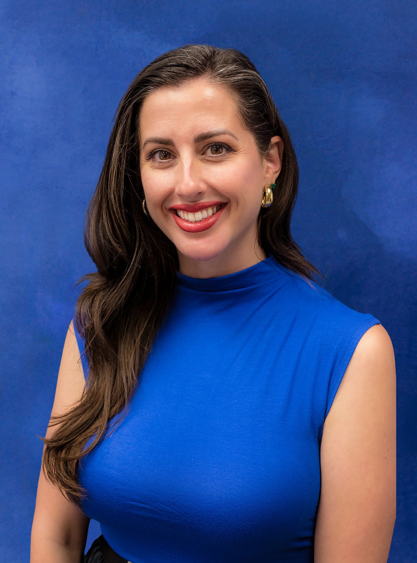 A woman with long dark hair, wearing a blue sleeveless top, smiling, against a blue background.