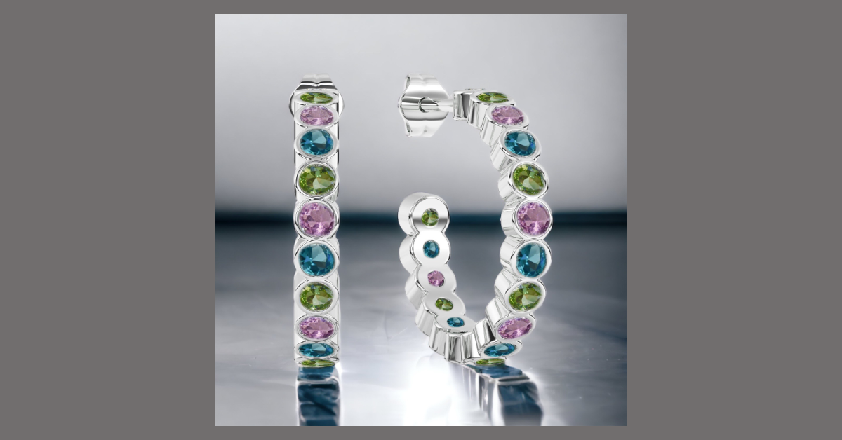 Silver hoop earrings with alternating pink, green, and blue gemstones on a reflective surface.