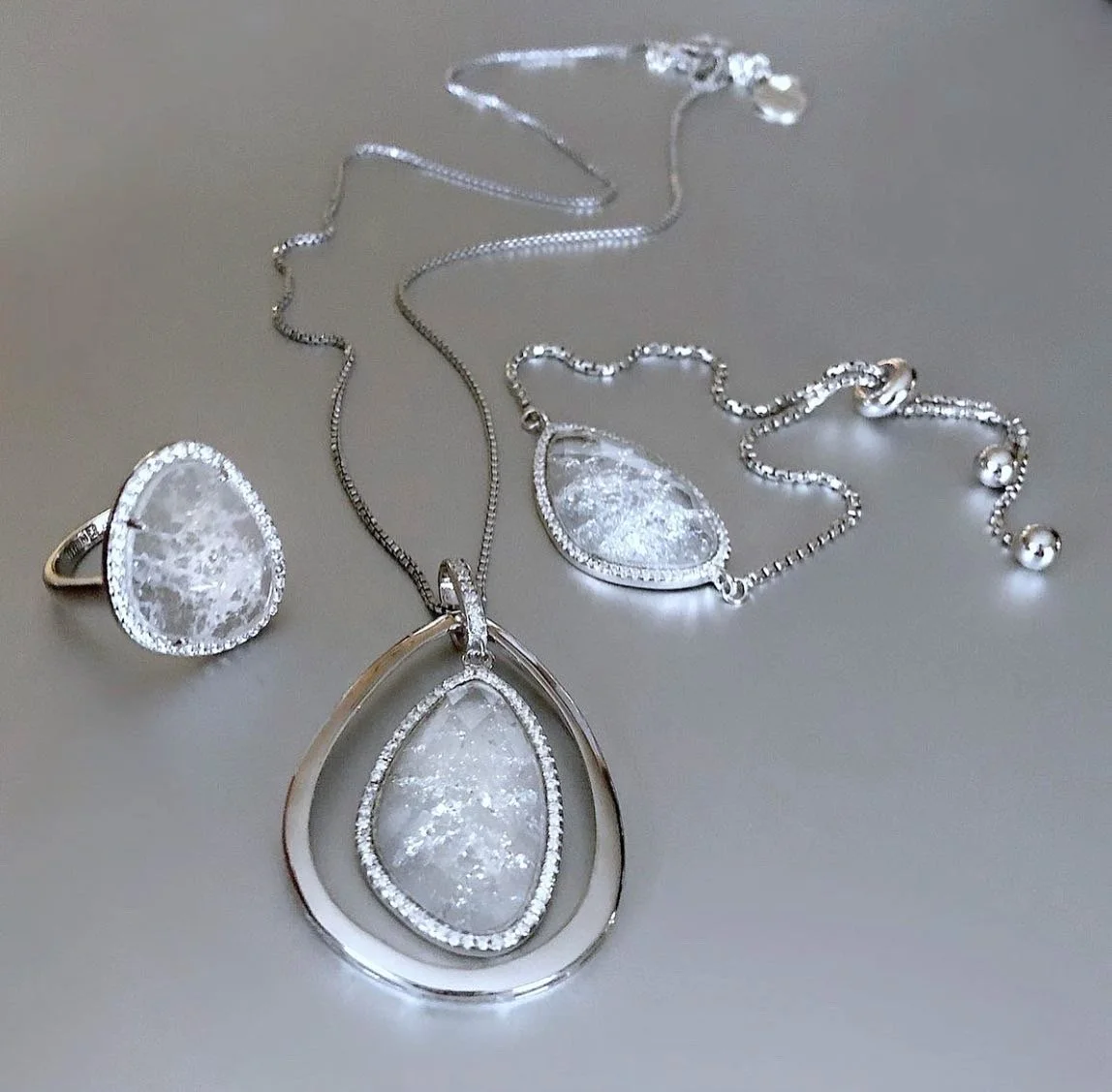Silver jewelry set with clear gemstones, including a ring, necklace, and bracelet.