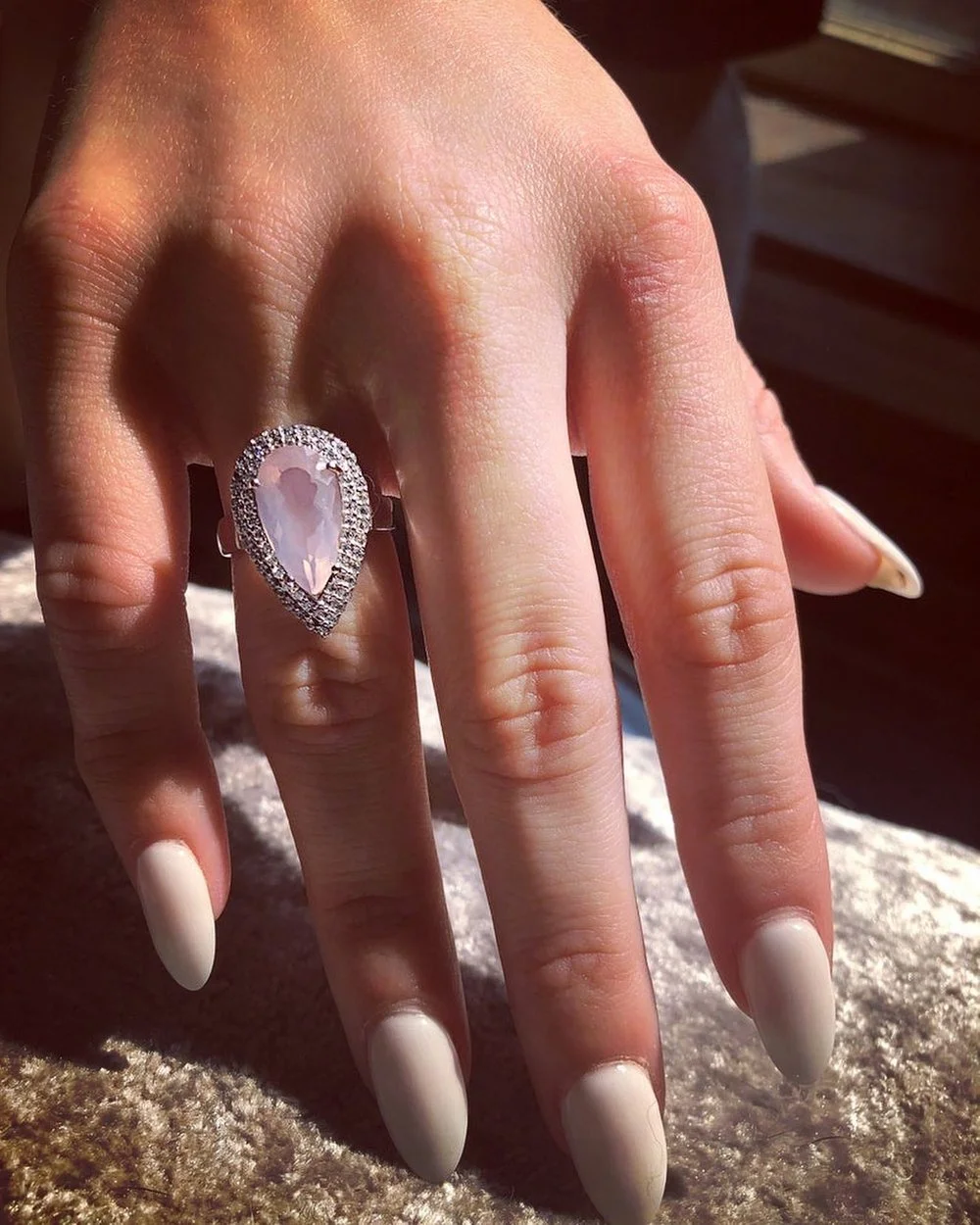 A close-up of a hand wearing a pear-shaped gemstone ring with a halo of smaller stones on the ring finger.