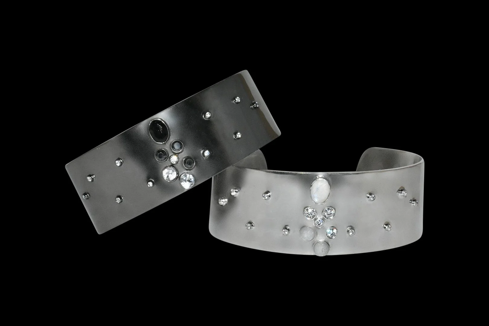 Two silver cuff bracelets with embedded gemstones on a black background.