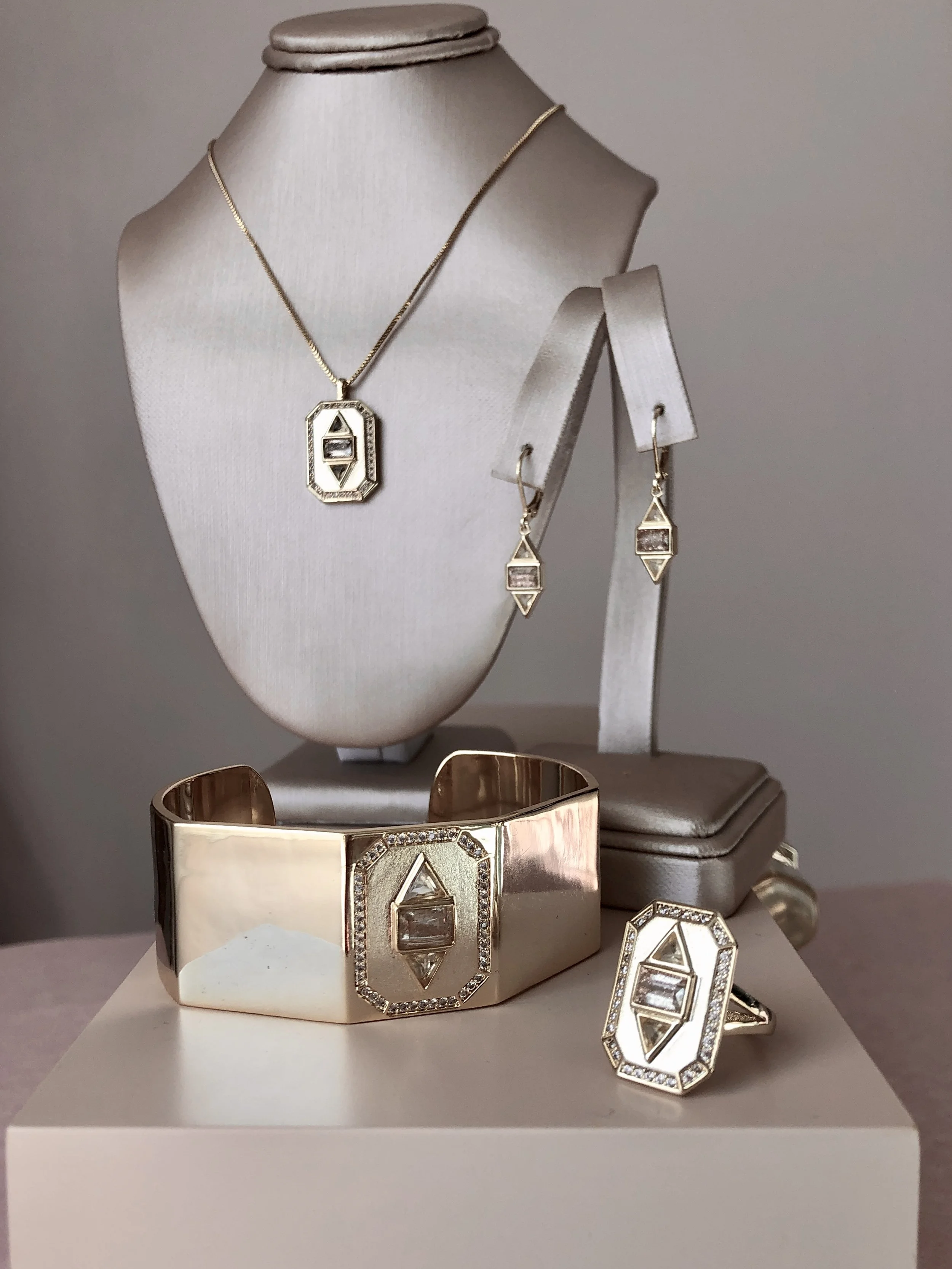 Jewelry set with necklace, earrings, ring, and bracelet featuring geometric diamond designs displayed on a stand.