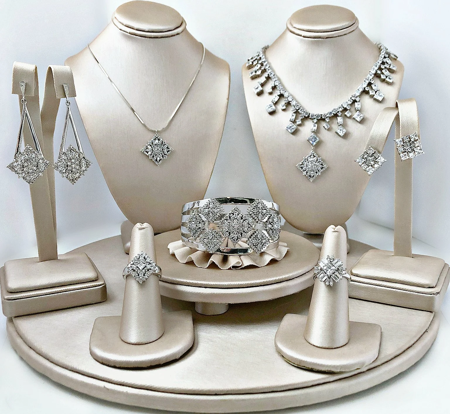Display of diamond jewelry including necklaces, earrings, rings, and a bracelet on beige stands.