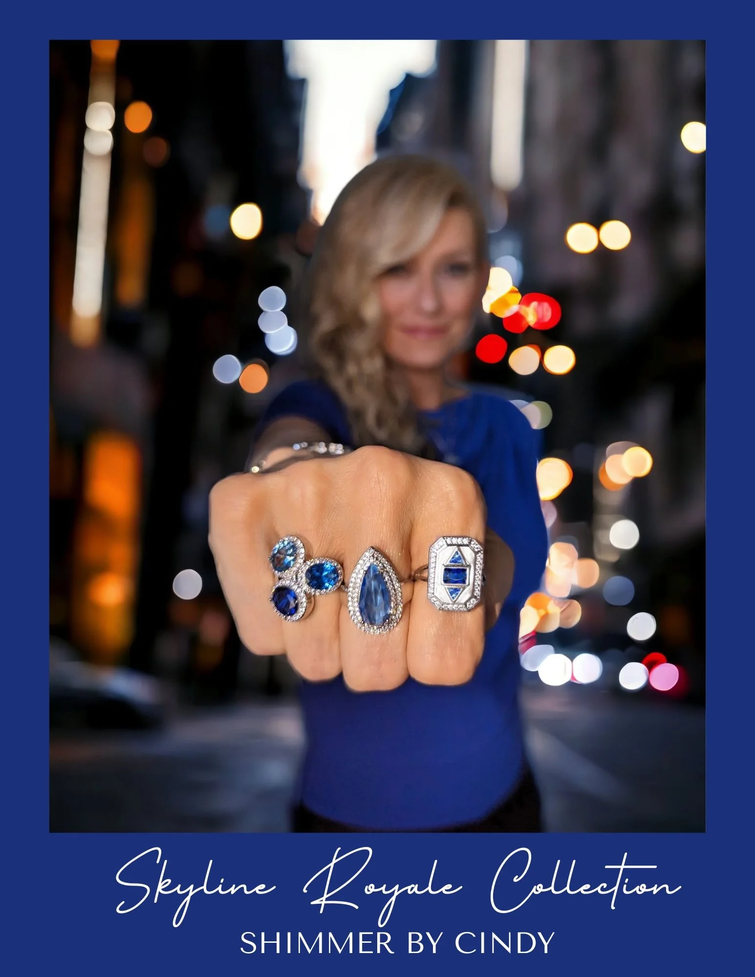 Close-up of three rings with blue gemstones worn by a person with blurred city lights in the background, featuring text 'Skyline Royale Collection Shimmer by Cindy.'