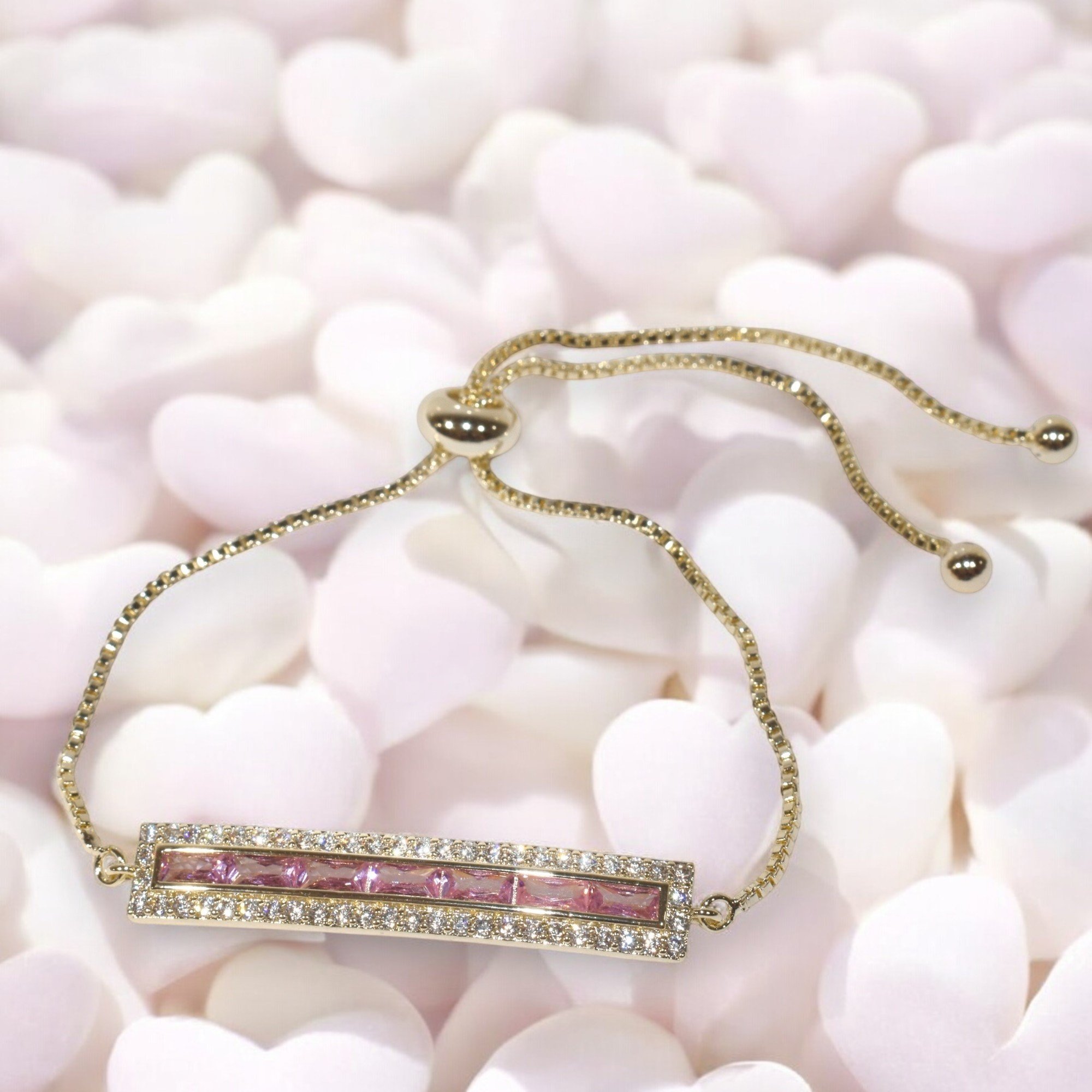 Gold bracelet with pink gemstones and diamond accents on heart-shaped background