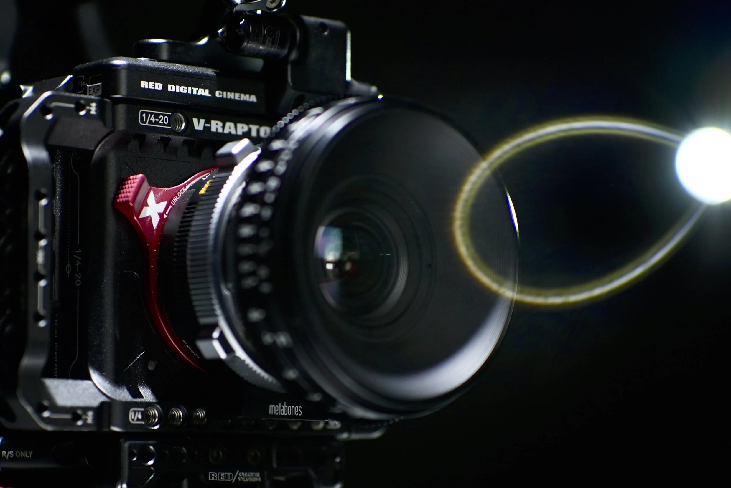 Close-up of a professional digital cinema camera with lens, set against a dark background with lens flare.