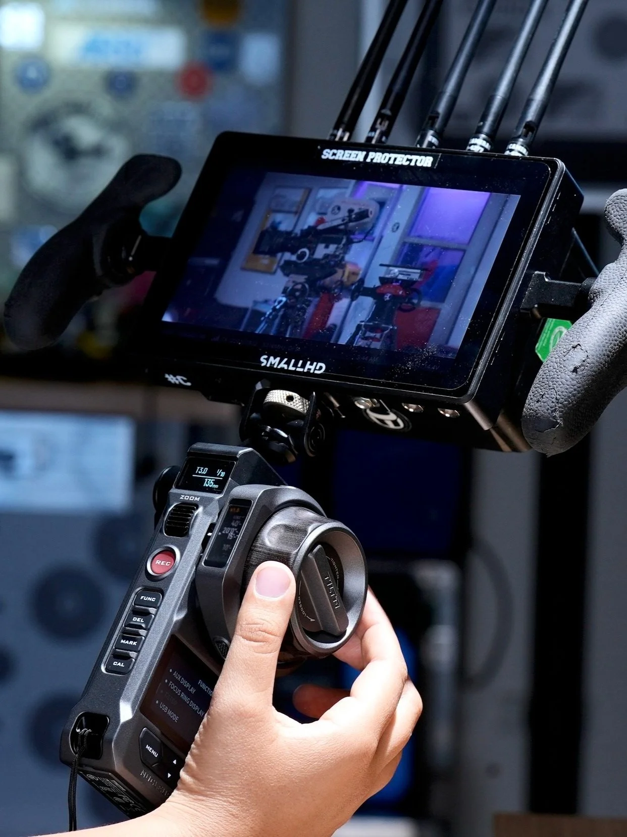 Close-up of a person operating a professional digital camera with a mounted monitor, inside a studio or workshop.