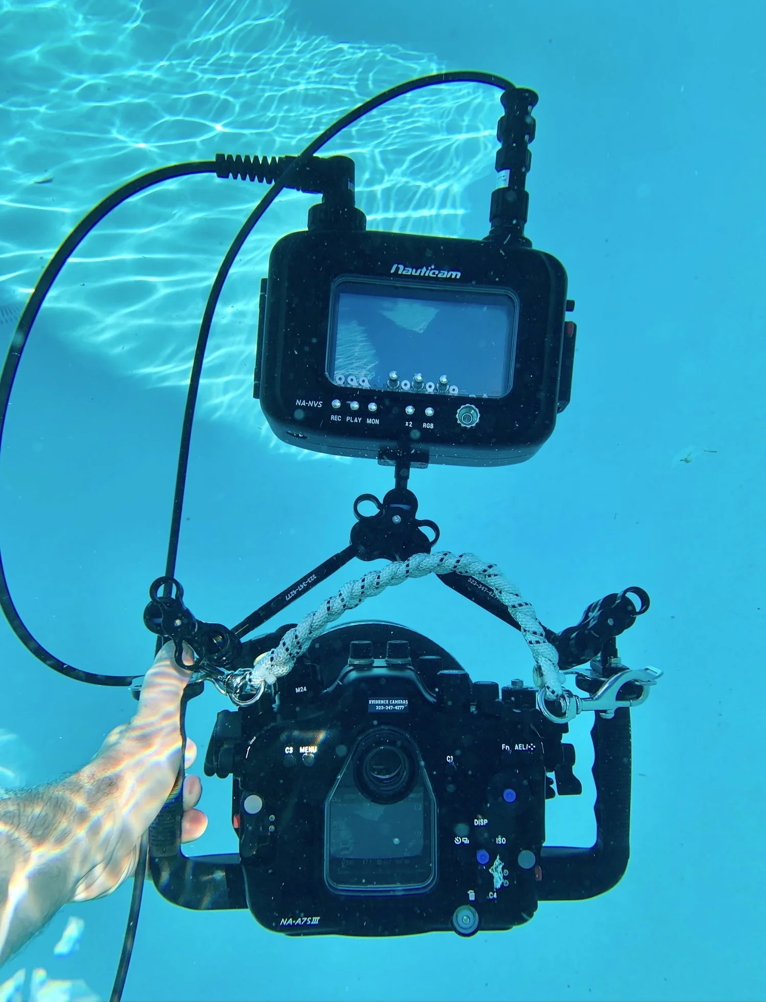 Underwater shot of a professional camera connected to an underwater monitor, capturing footage in the ocean.