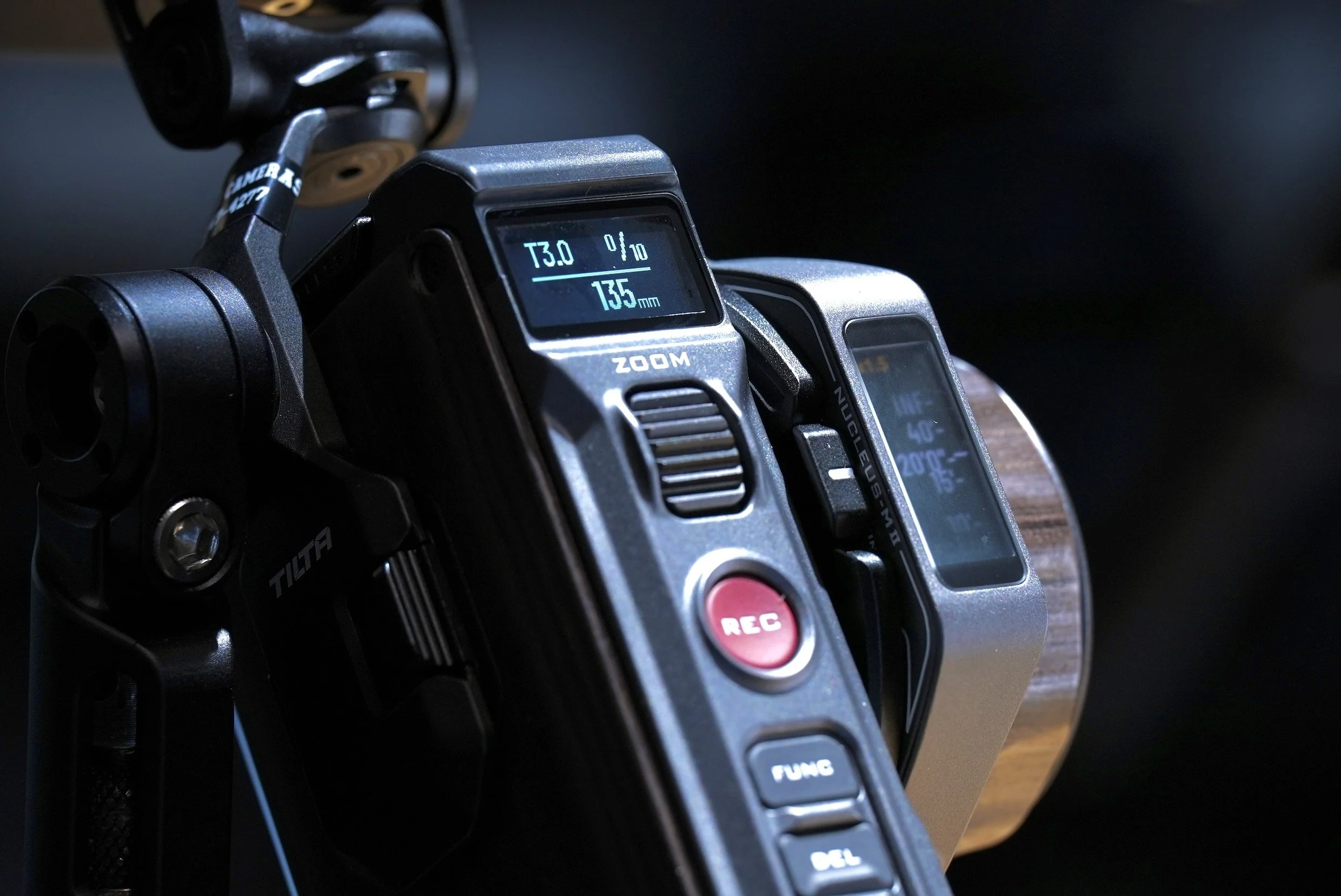 Close-up of professional video camera with digital display showing focus distance, zoom level, and other settings.