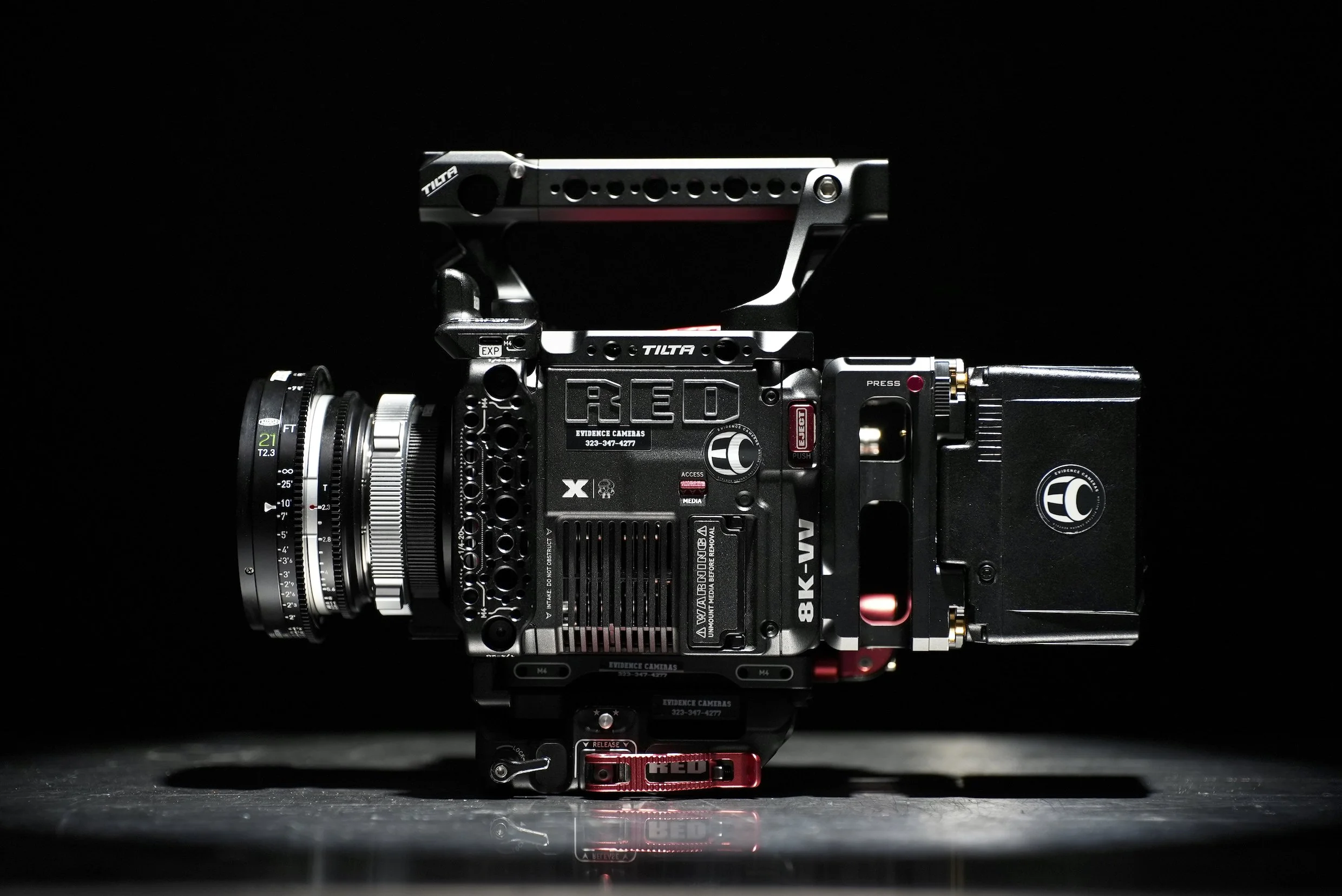 A professional cinema camera mounted on a detailed support rig, set against a black background with reflective surface.