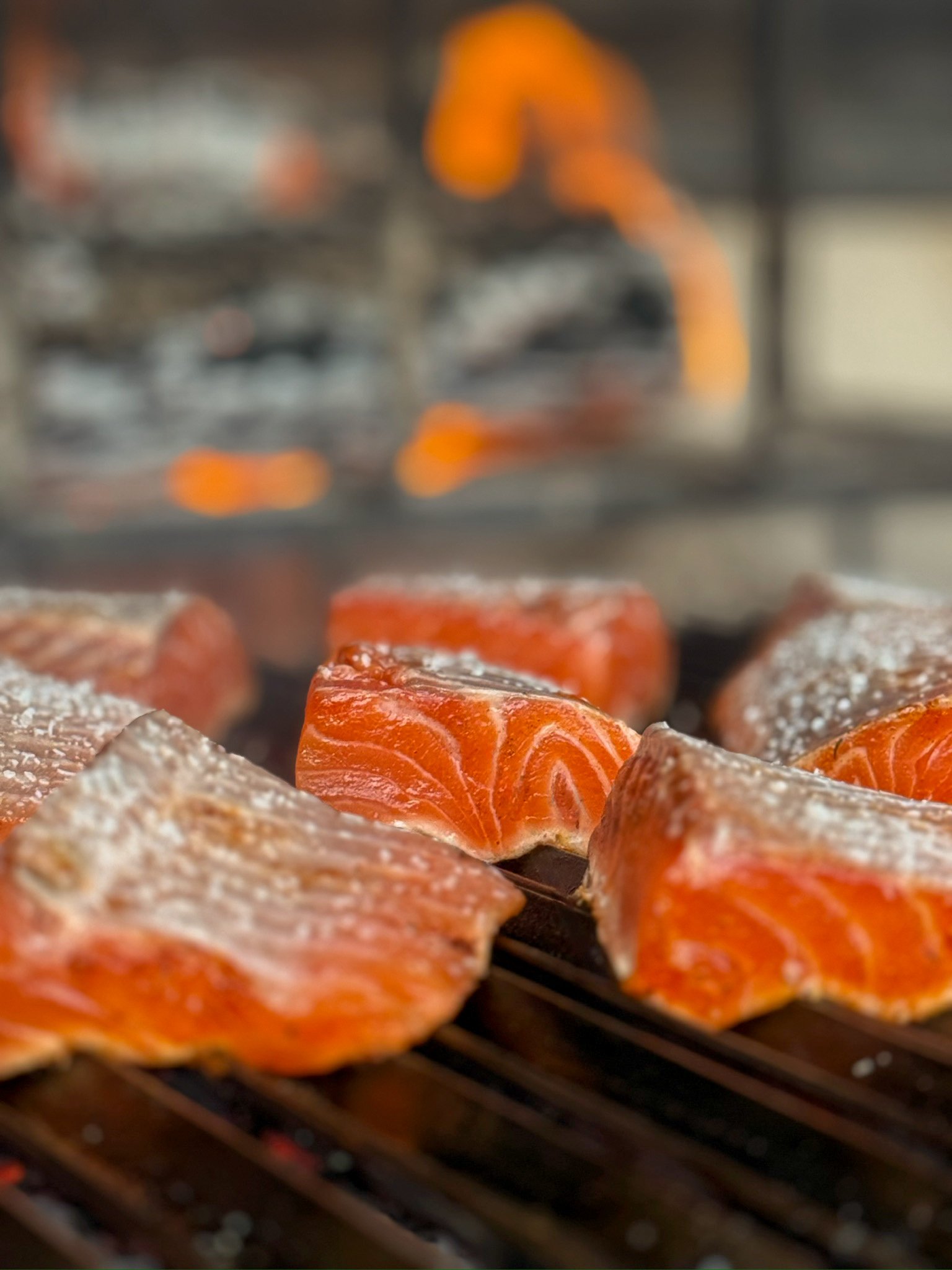 Faroe Island salmon cooking skin-side down on a parrilla grill over live fire.