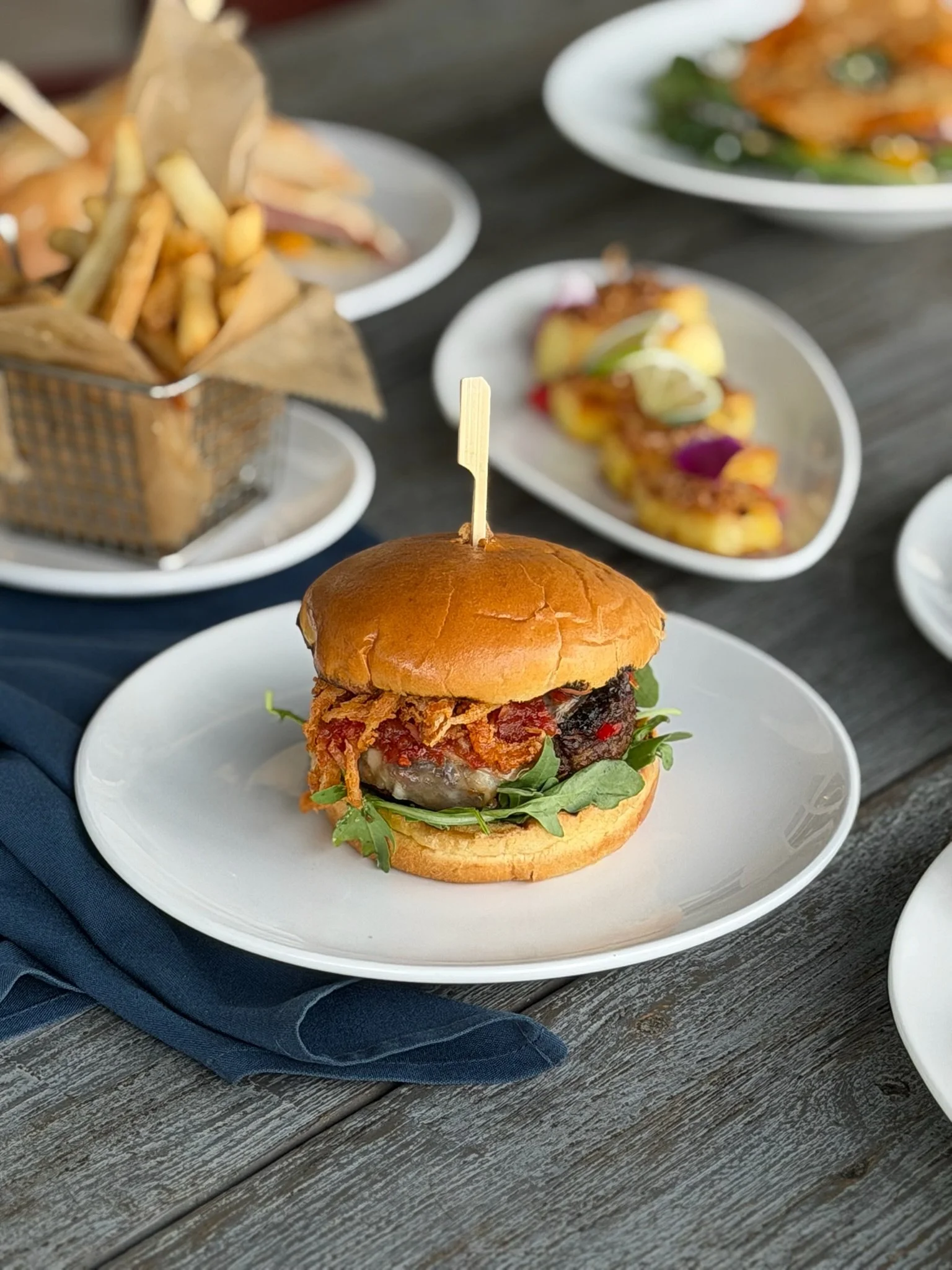 Gaucho burger plated with a side of fries and a pineapple appetizer in the background