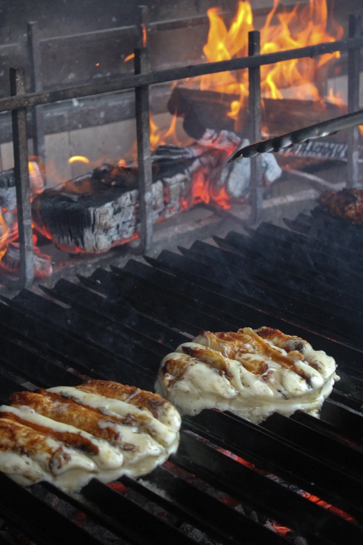 Provoletta grilling over an open flame, with fire in the background highlighting the live-fire cooking technique.