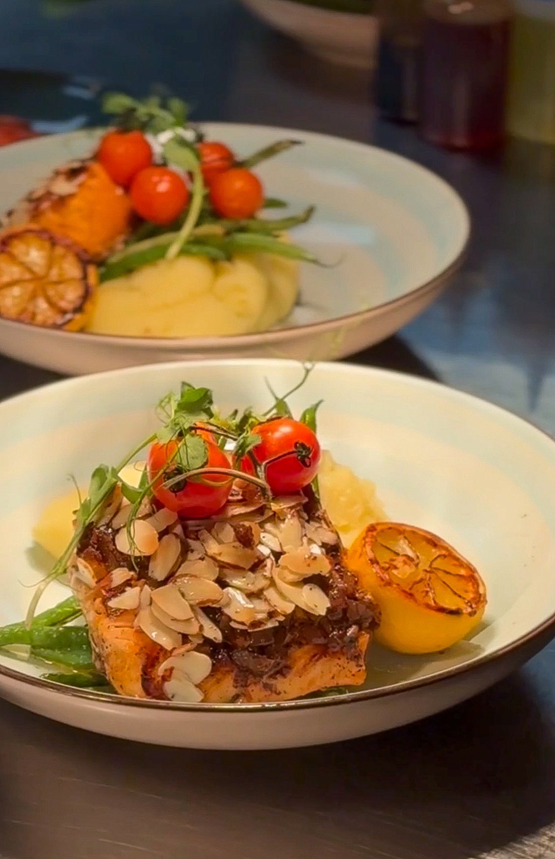 Grilled Faroe Island Salmon Almondine plated with Yukon Gold potato mousseline, haricot verts, toasted almonds, melted tomatoes, and citrus–shallot–thyme brown butter.