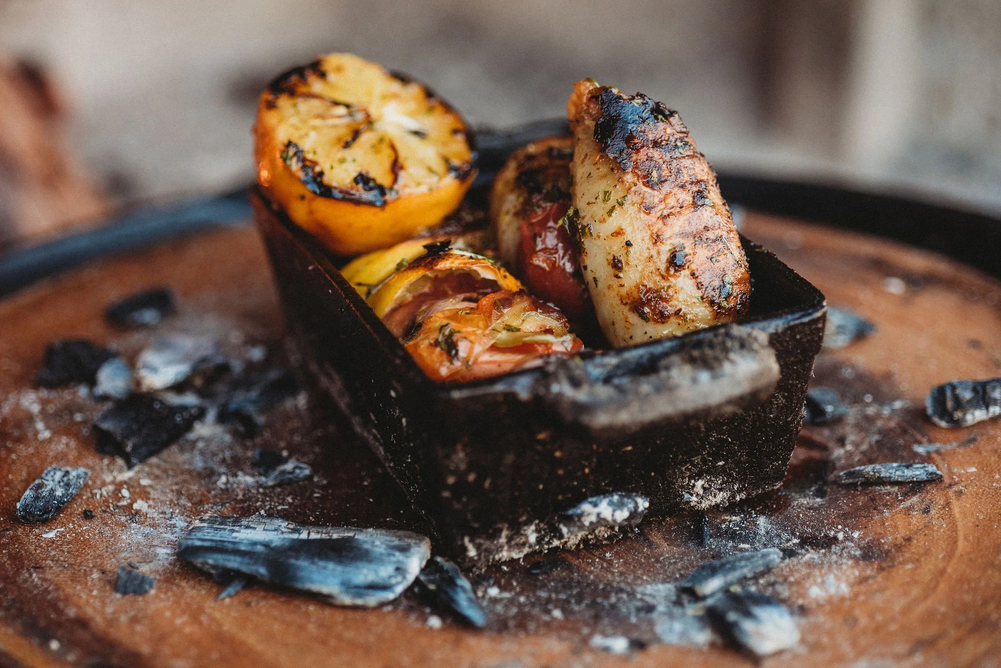 Shrimp, house-made chorizo del mar, and salsa criolla in a cast iron pan surrounded by coal