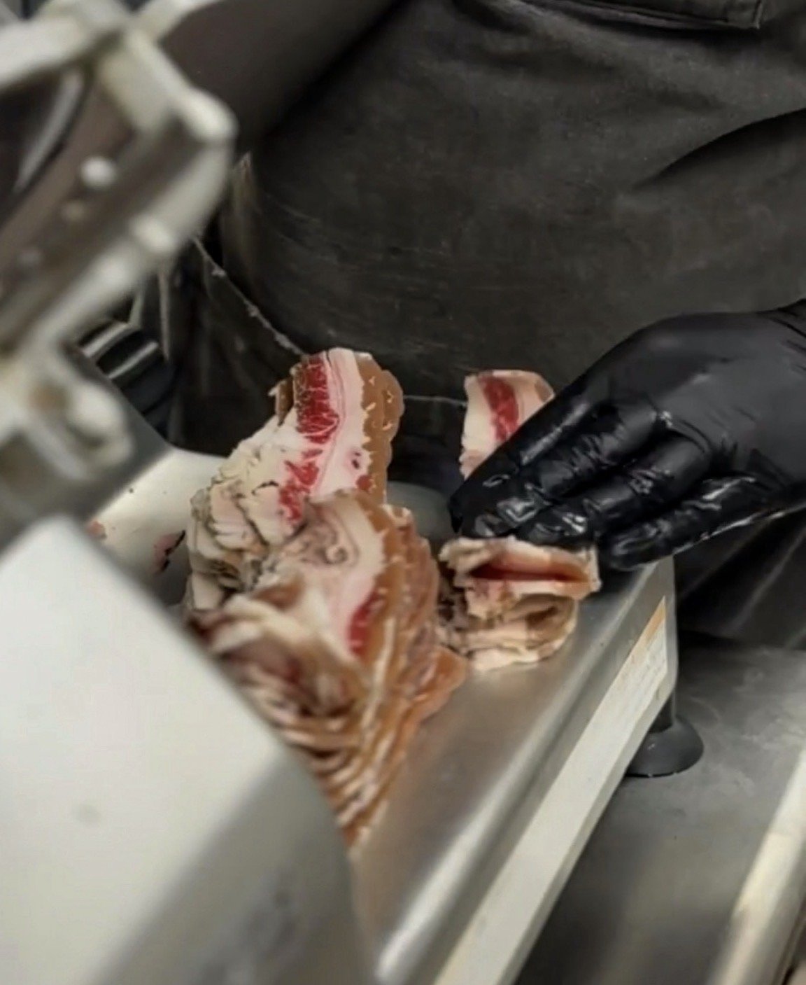 Housemade beef bacon being sliced on a commercial meat slicer in a restaurant kitchen.