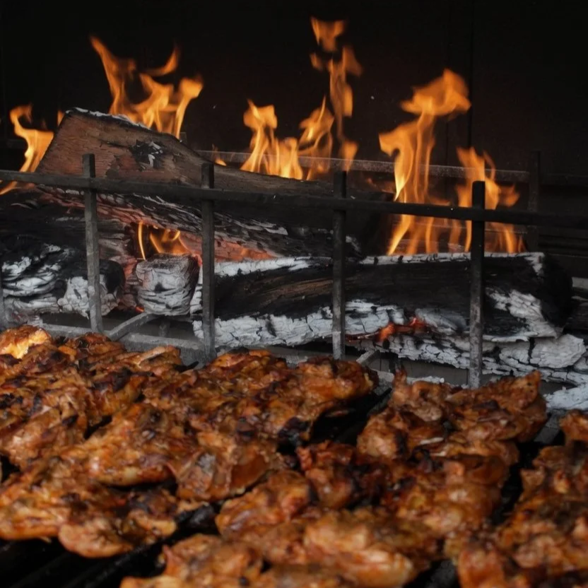 Signature spiced chicken thigh cooking over live fire on an Urban Asado grill at Asado Life.