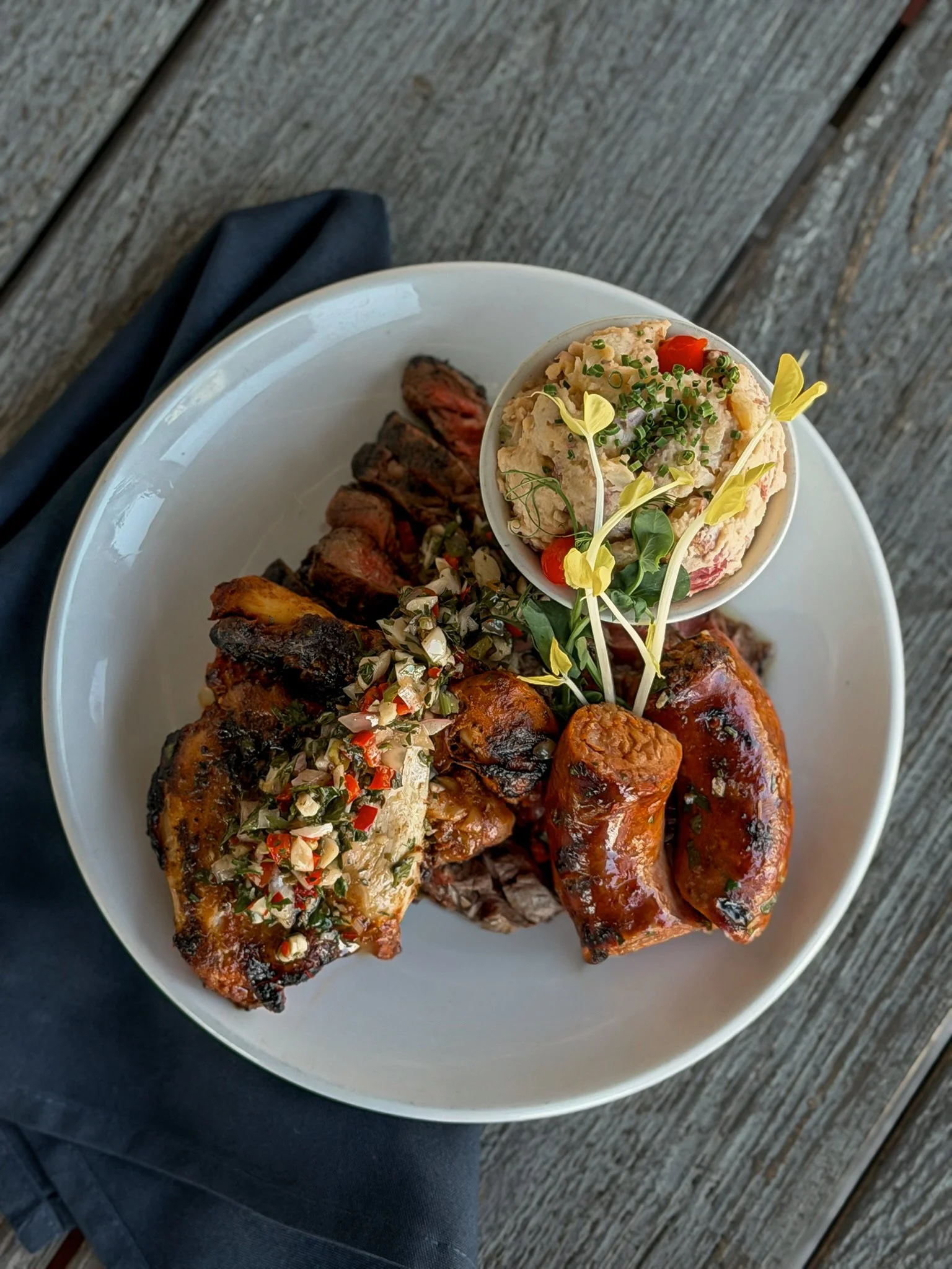 A plated fire-grilled entrée at Asado Life topped with vibrant green housemade chimichurri. The fresh herb sauce adds a bright pop of color against the grilled meat, highlighting the dish's fresh, Argentine-inspired flavors.