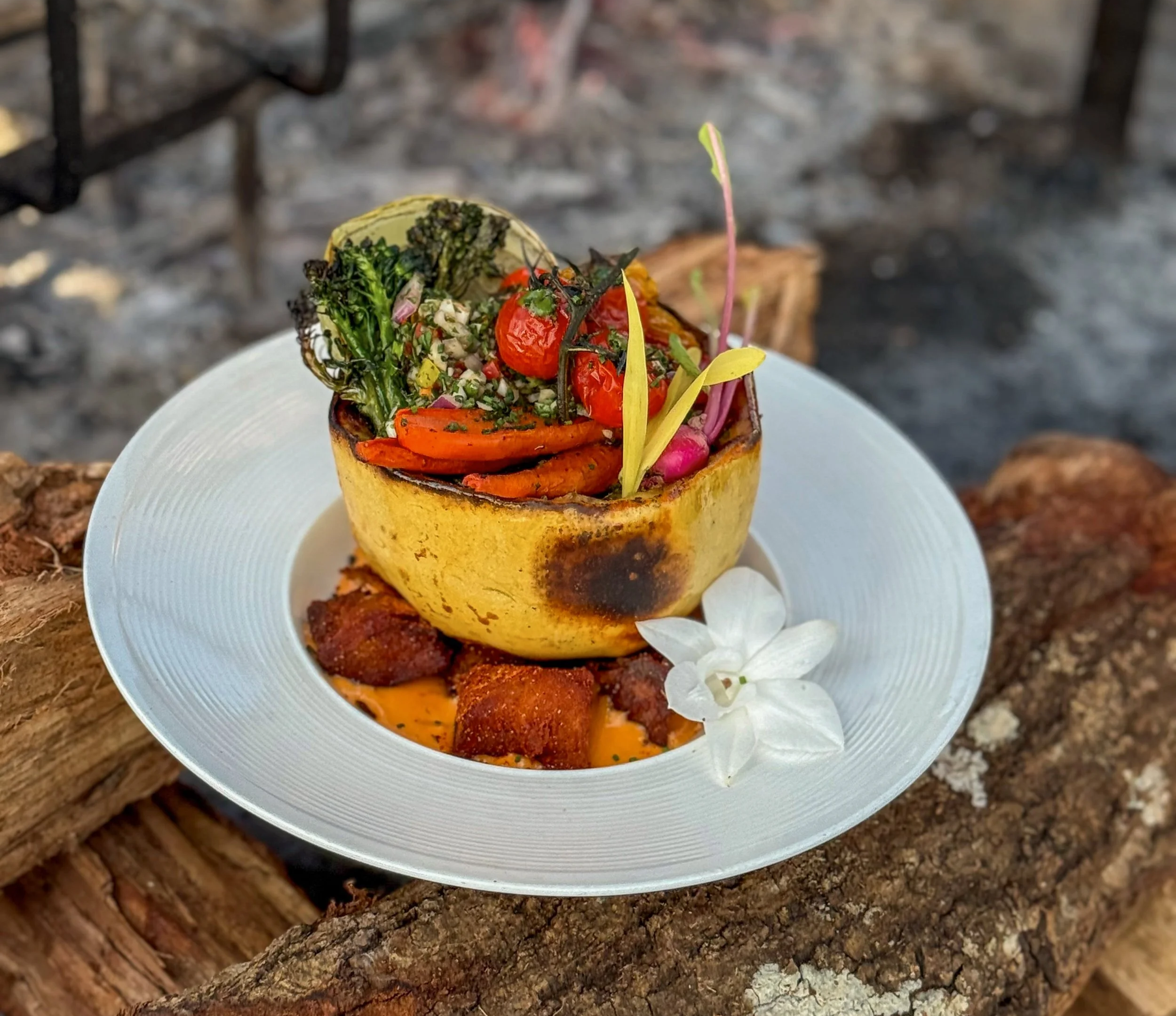 Plated ember-roasted spaghetti squash with parrilla-grilled vegetables plated over a grill at Asado Life.