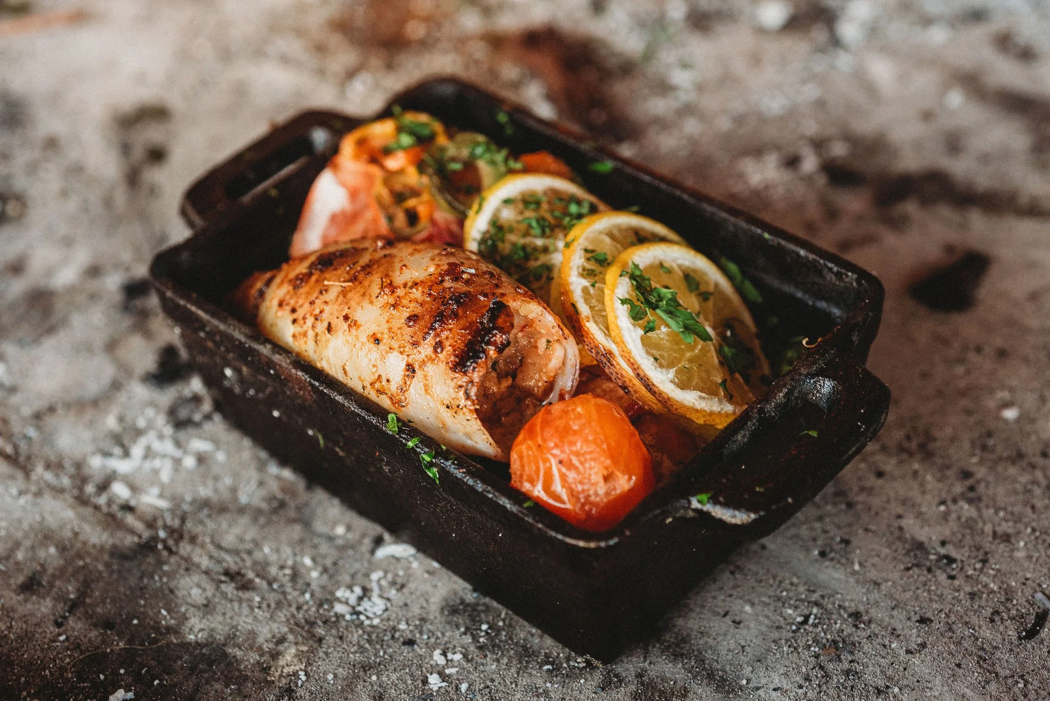 Shrimp, house-made chorizo del mar, and salsa criolla in a cast iron pan surrounded by coal