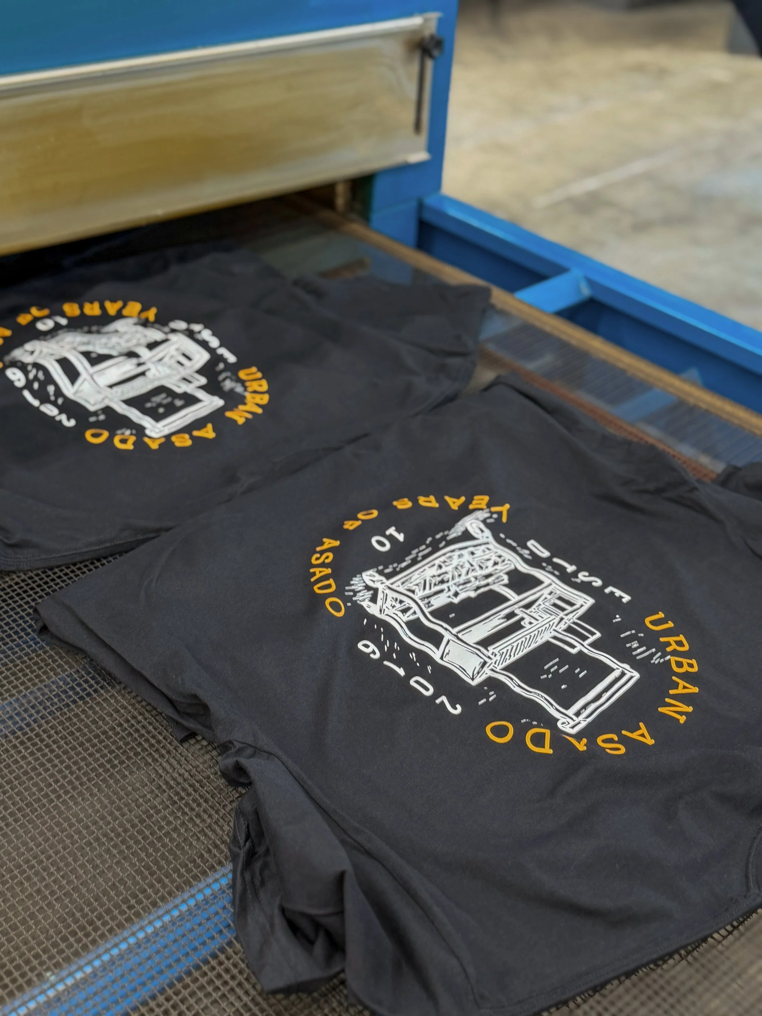 Urban Asado 10-year anniversary shirts moving through a drying roller at Sports Corner in St. Augustine.