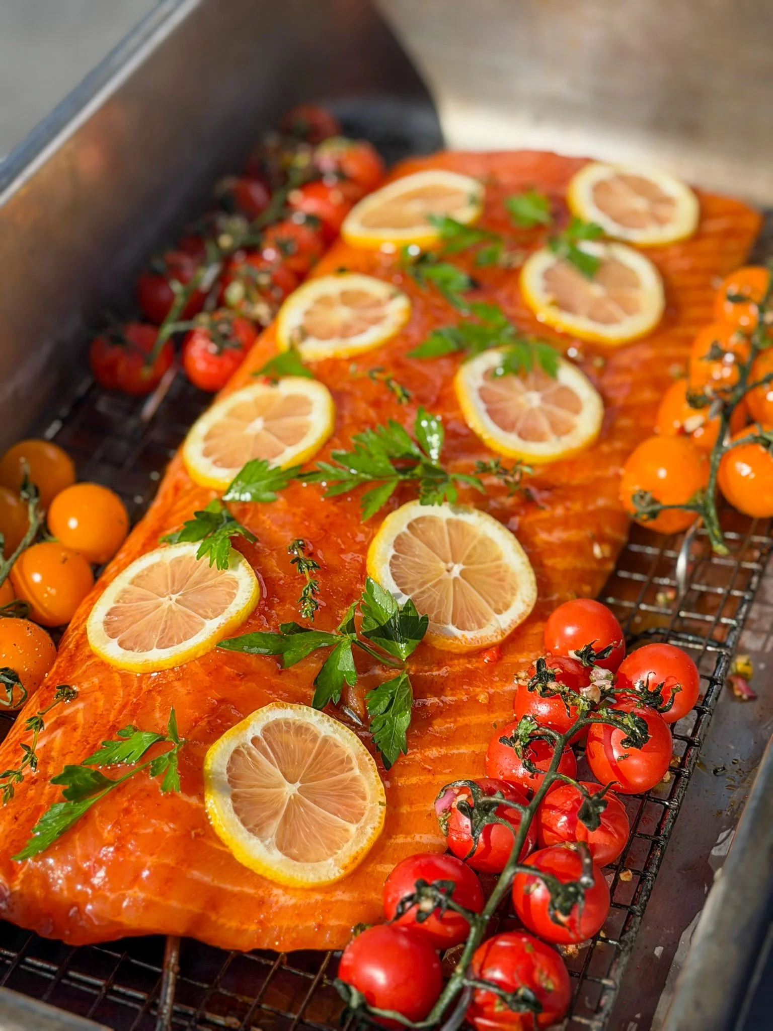 Raw Faroe Island salmon on an expanded metal grilling cage with fresh lemon slices and tomatoes, prepared for live-fire cooking.
