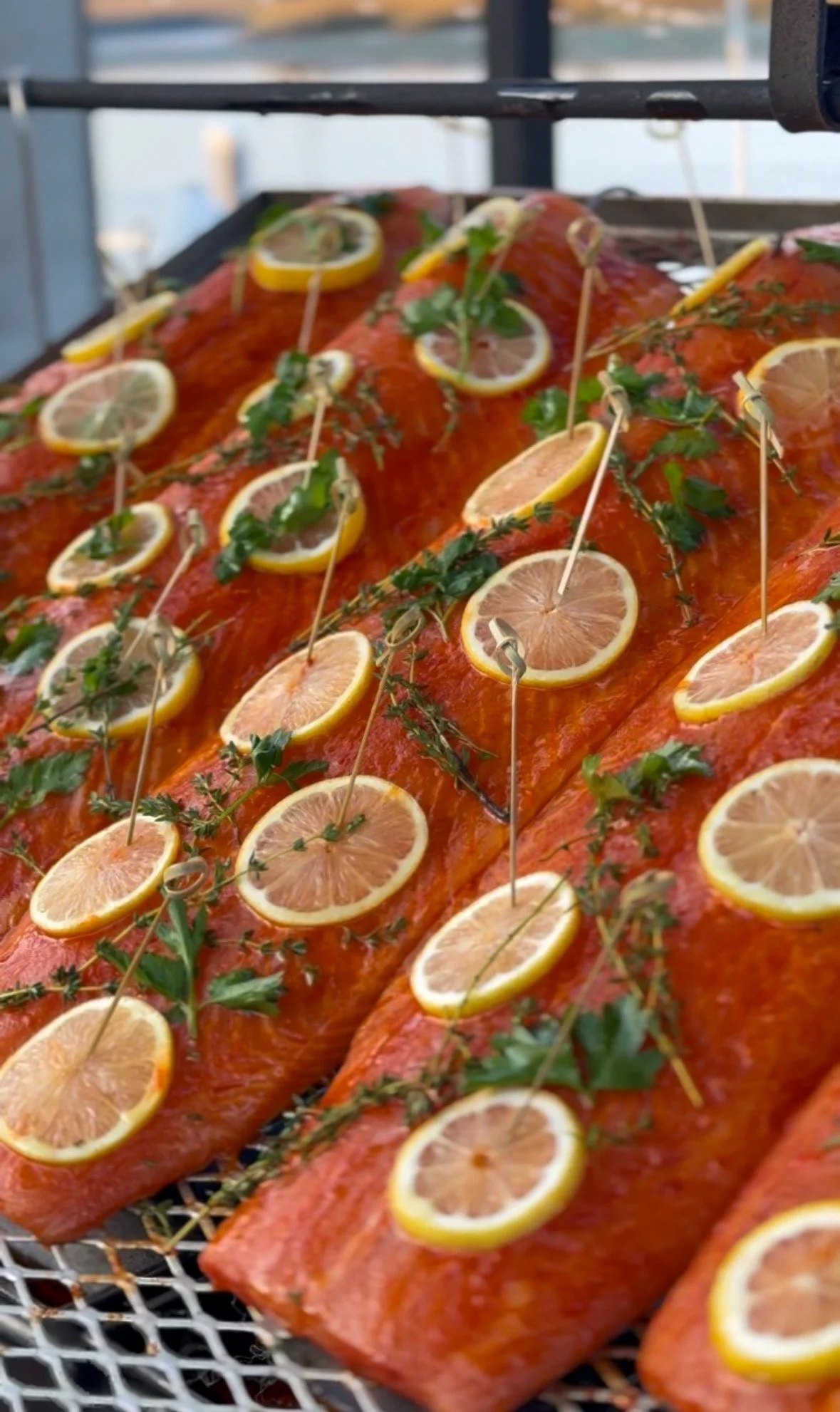 Raw Faroe Island salmon on an expanded metal grilling cage with fresh lemon slices and tomatoes, prepared for live-fire cooking.