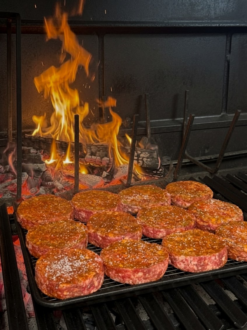 Burger patties cooking over a live fire parrilla grill