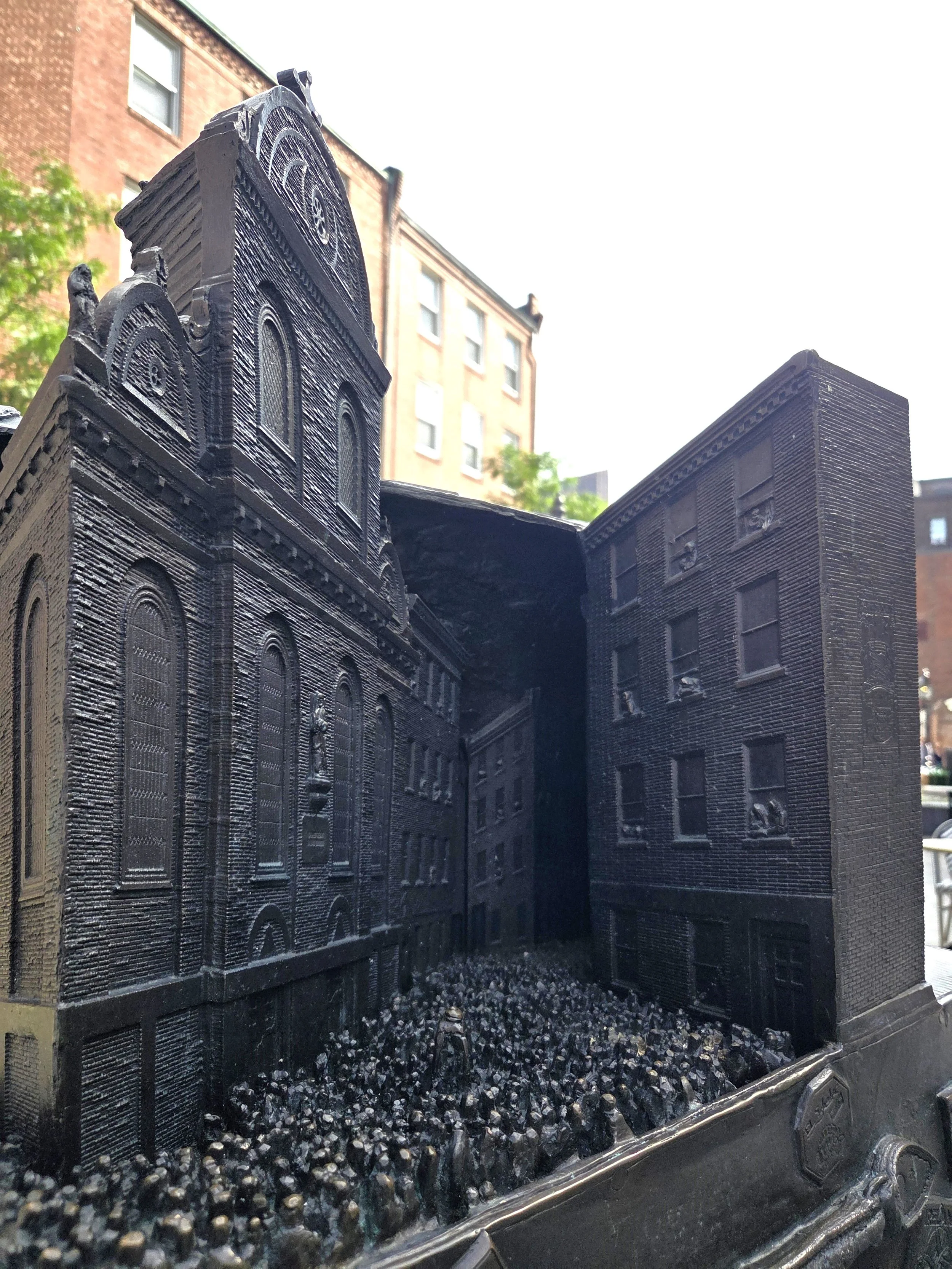 small depiction of the Sacred Heart Church with its arched silhouette. In front is a crowd celebrating a feast and parade with a catholic saint.