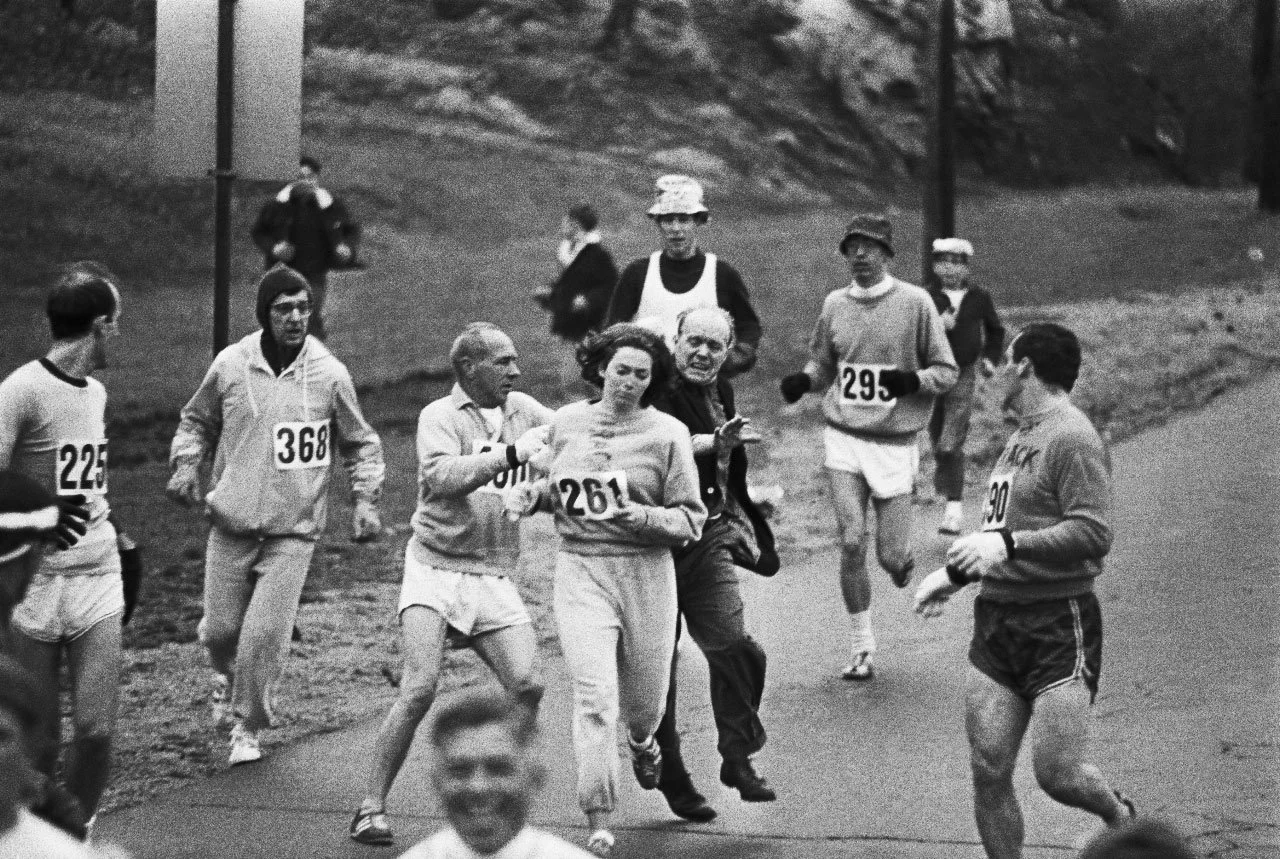 Kathrine Switzer running while race administrators attempting to grab her mid-race