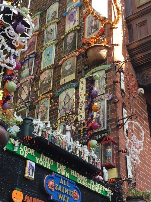 All Saints Way shrine with portraits and prayer cards on brick walls