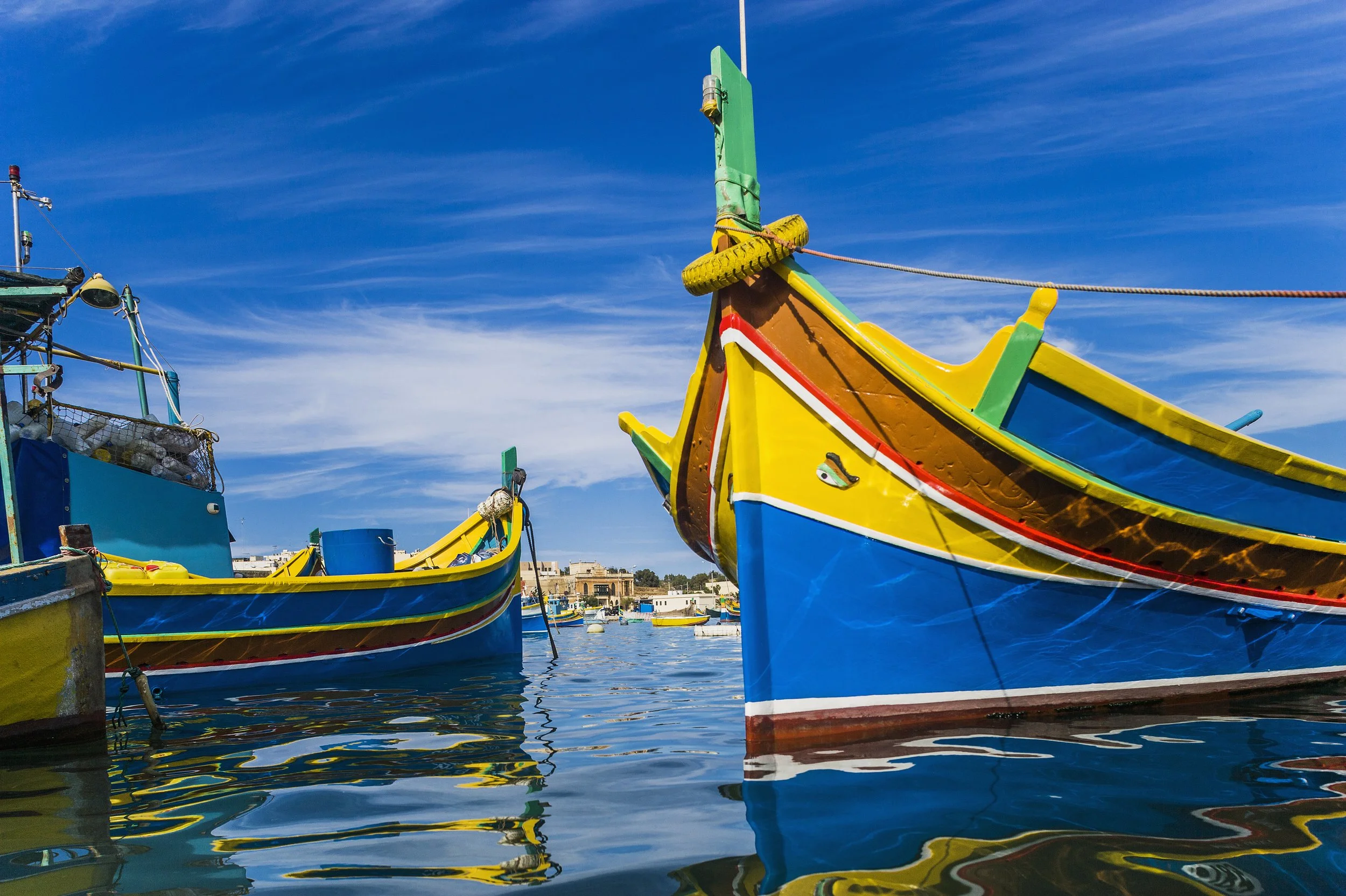 Colorful traditional Maltese fishing boats docked in the harbor under a blue sky.